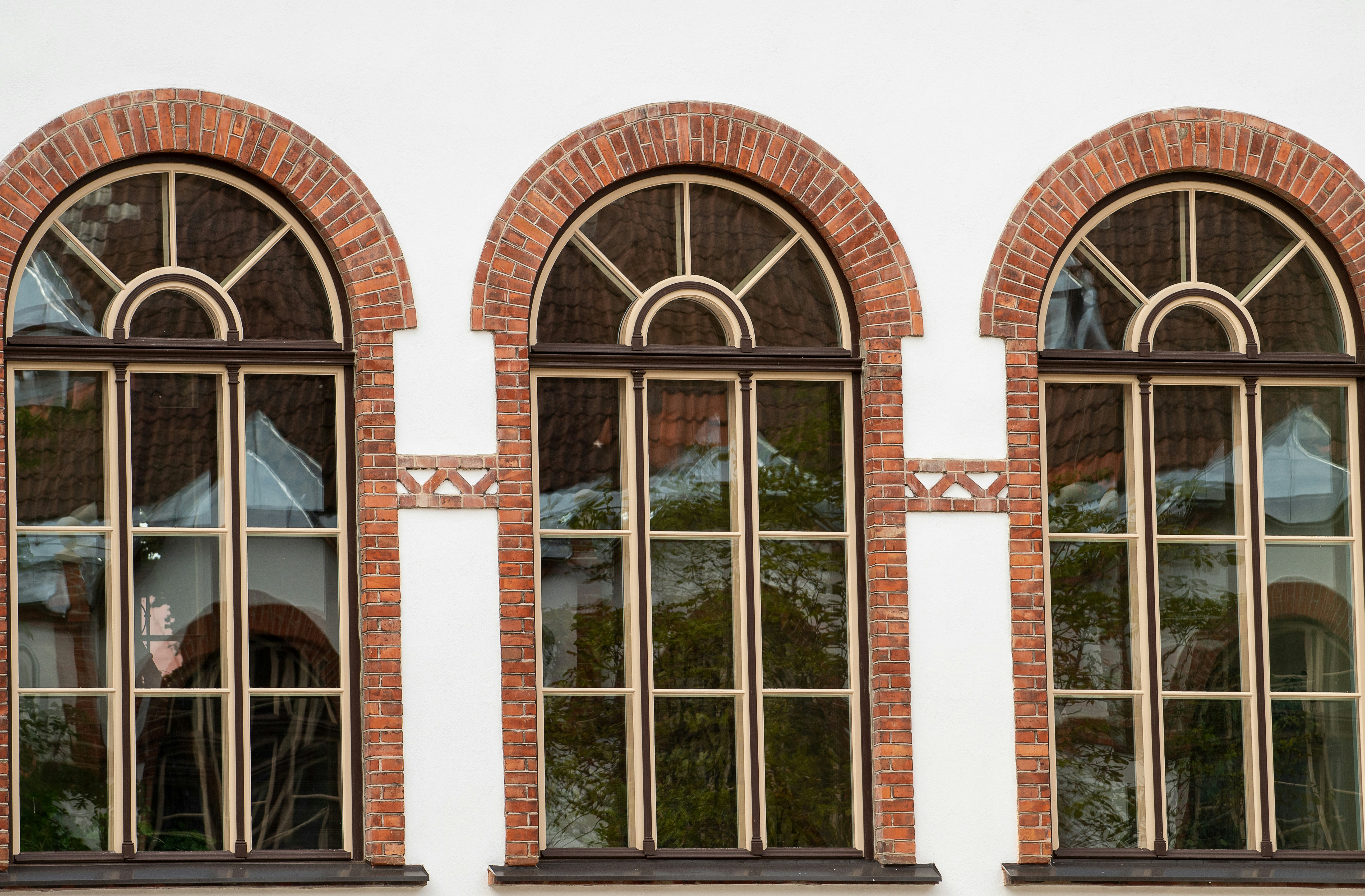 Three arched windows with brick frames on a white building.