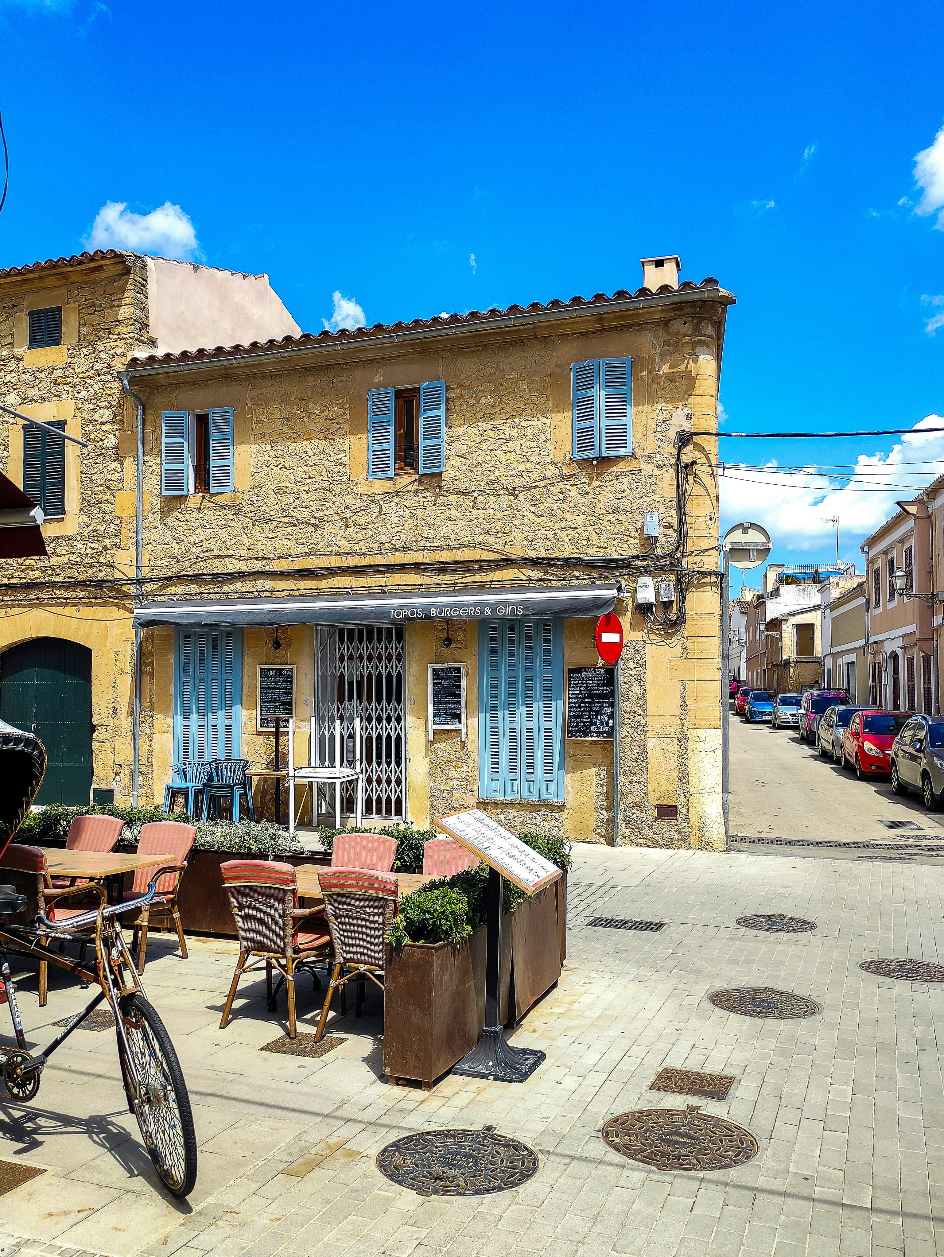 A stone building with blue shutters and an outdoor cafe.