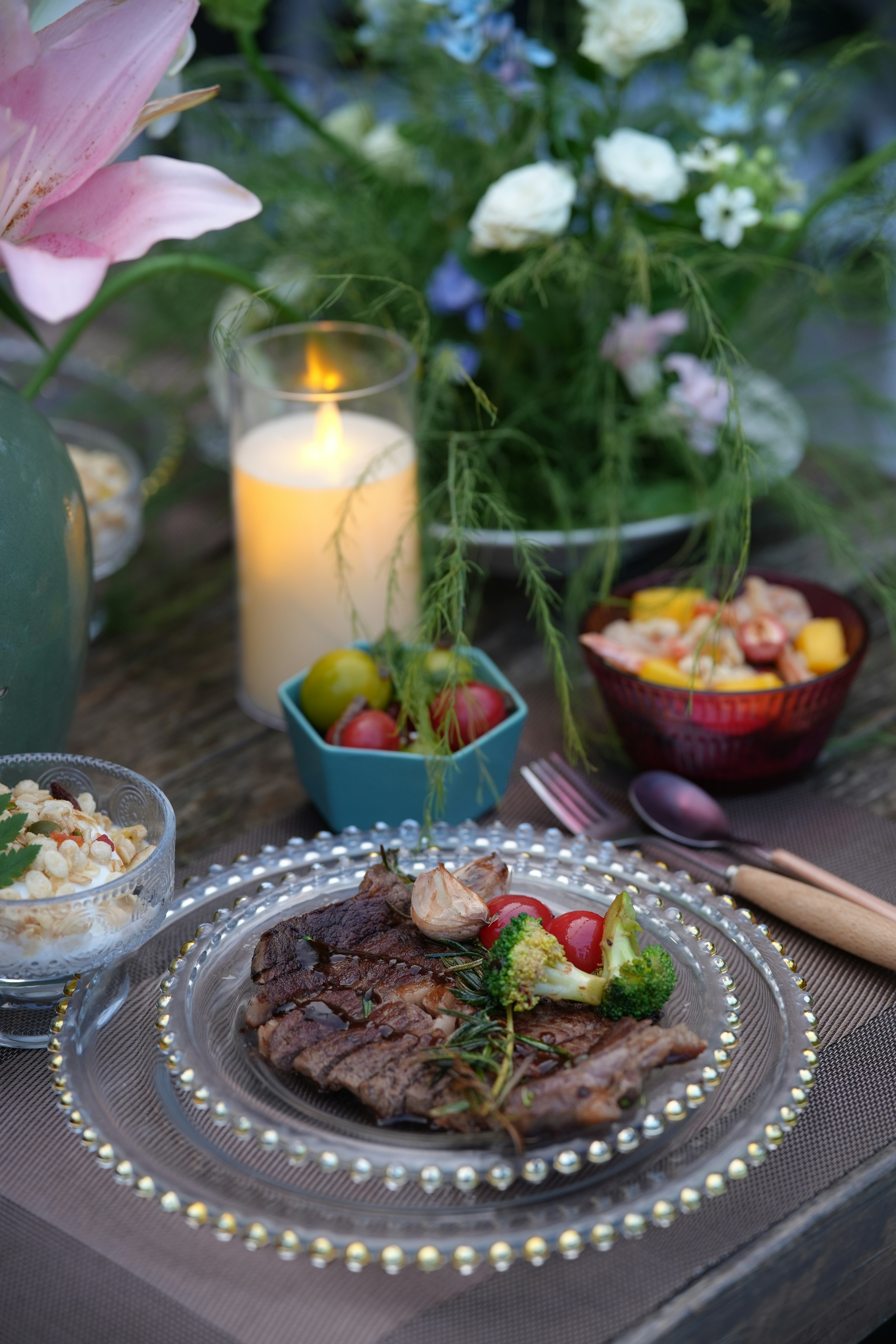 Grilled steak dinner with candle and floral decorations.