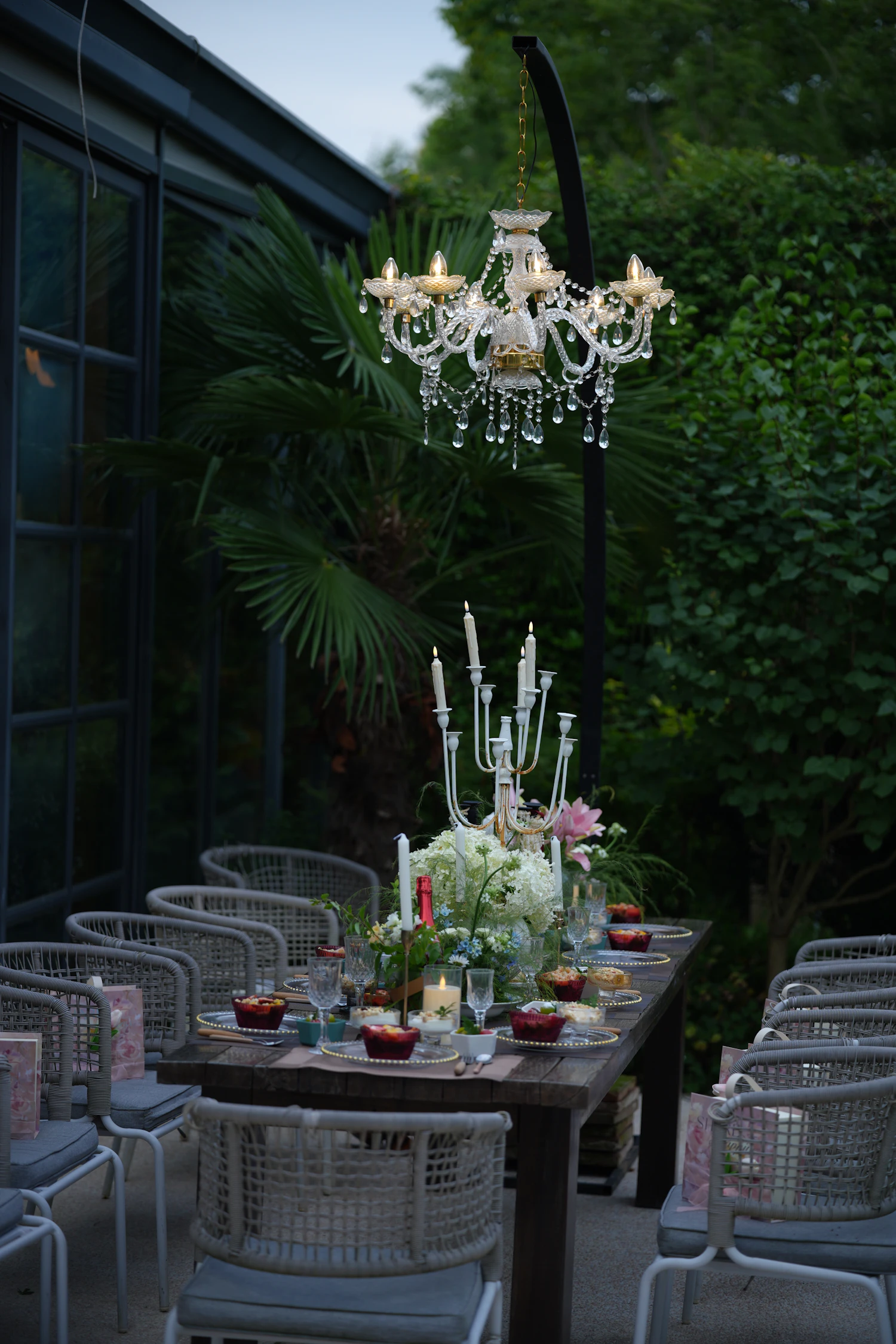 A long table laid under a chandelier hung in a wall of greenery at night