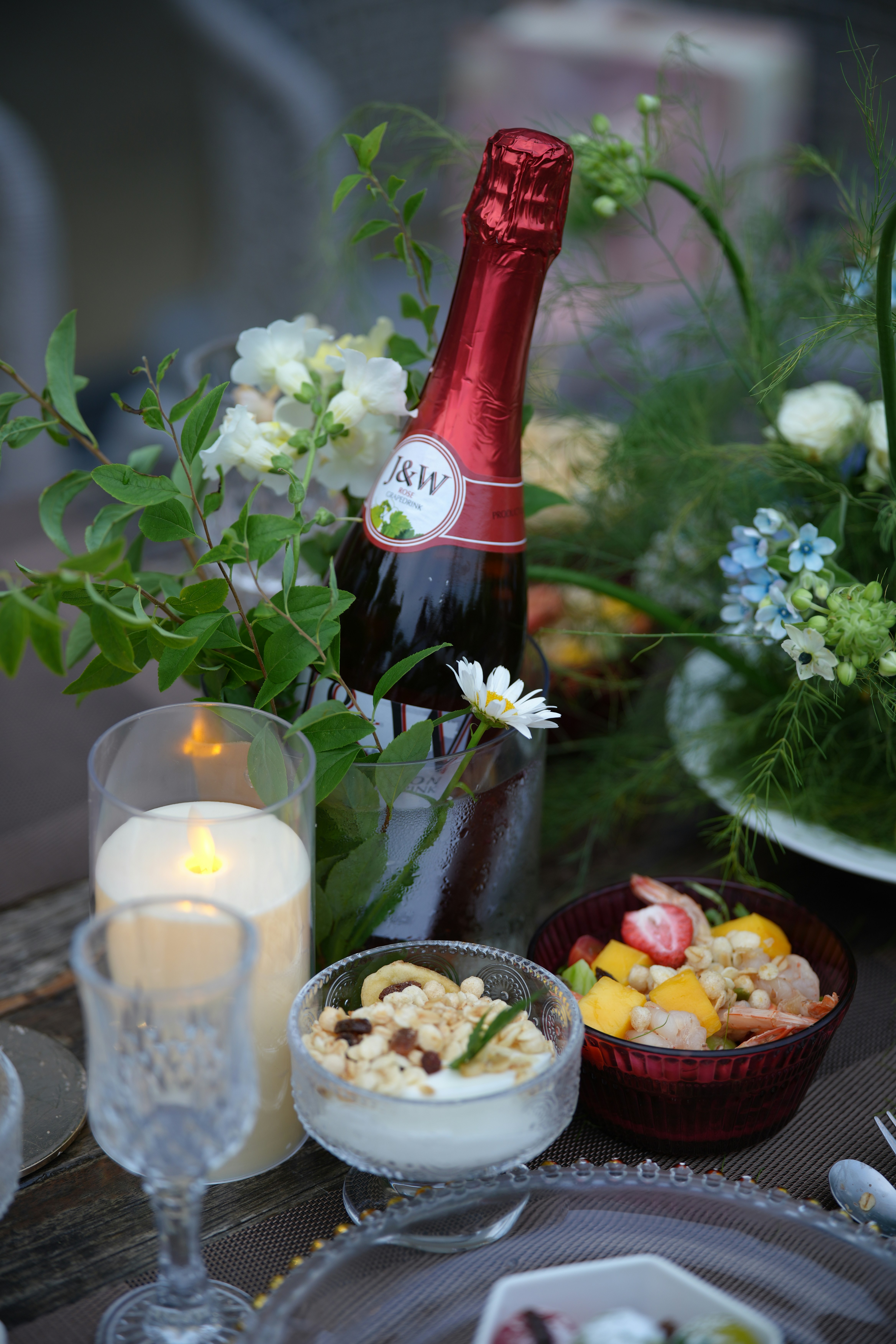 Elegant table setting with champagne, candle, fruit, and flowers.