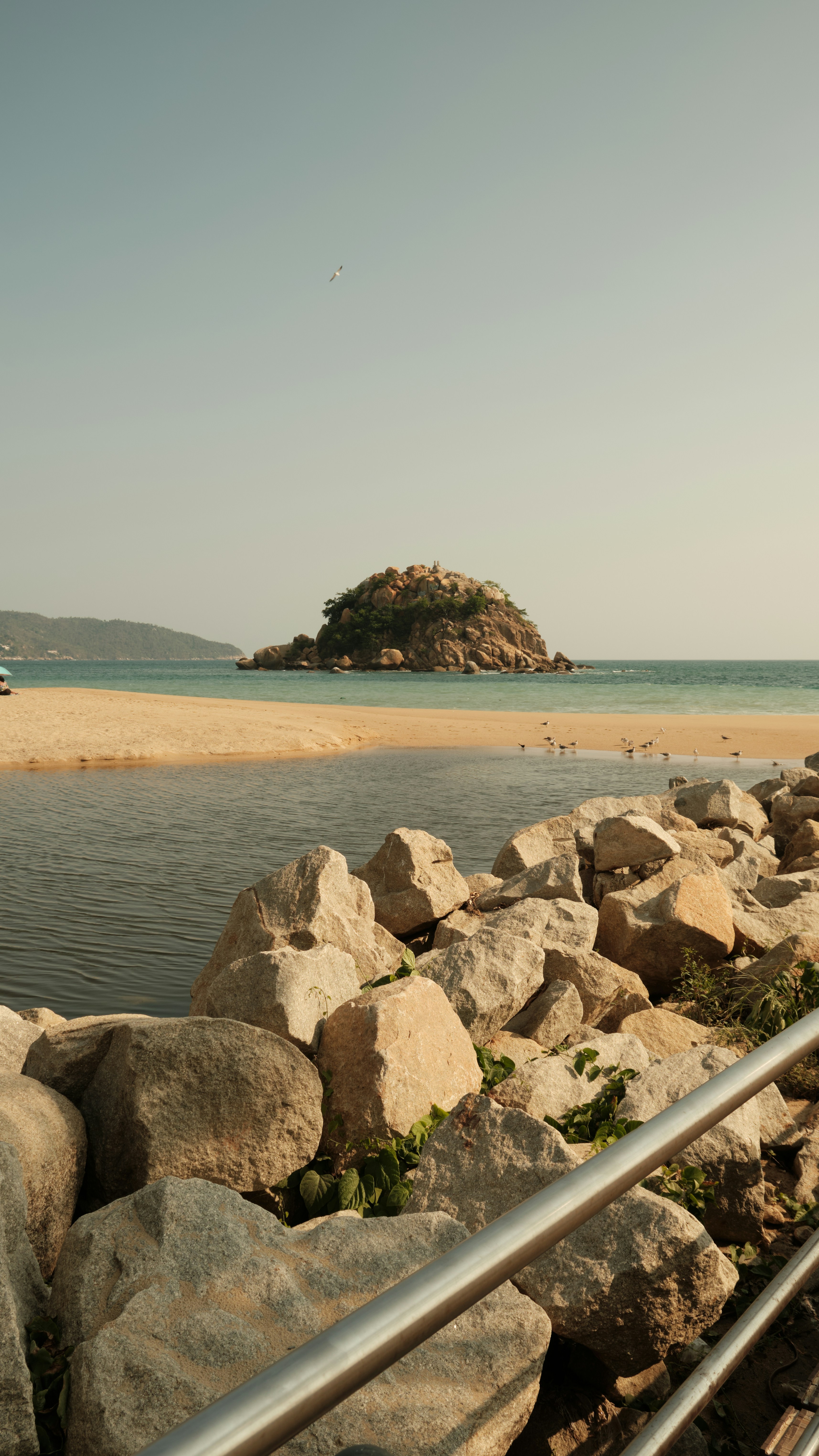 Small rocky island offshore from a sandy beach.