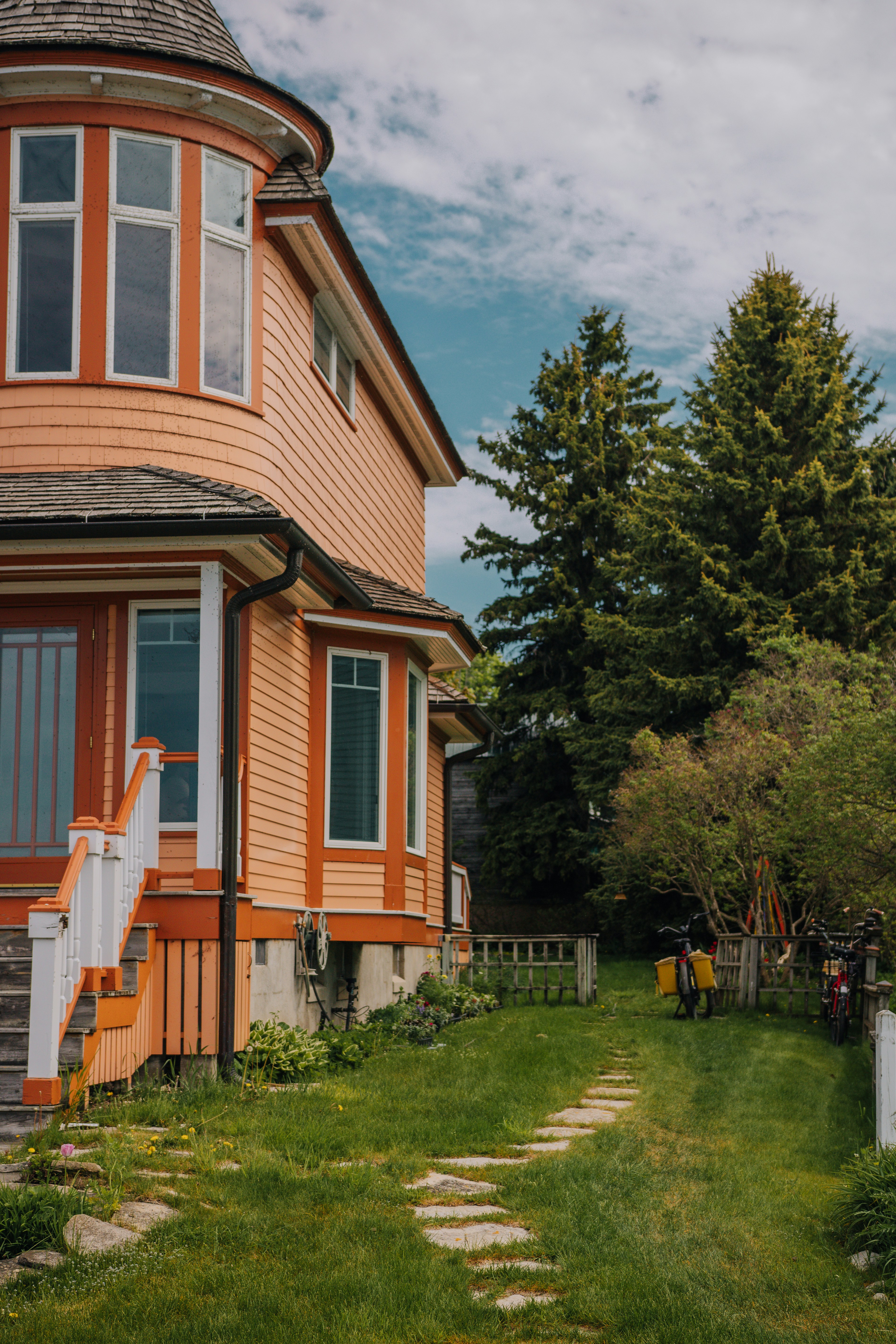 Orange house with white stairs, green lawn, and tall trees