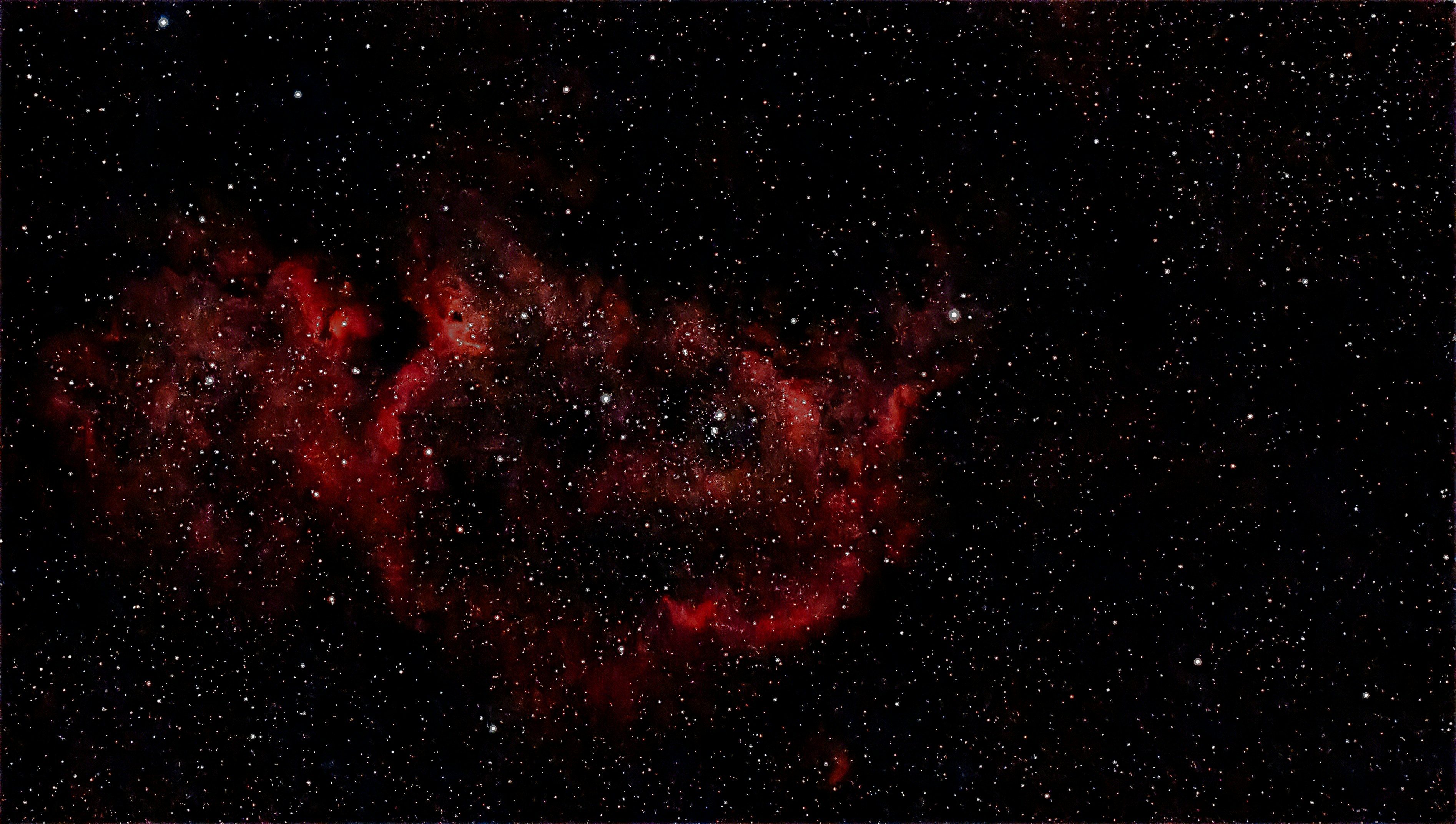 Nebula merah bersinar terang di kosmos yang gelap dan dipenuhi bintang.