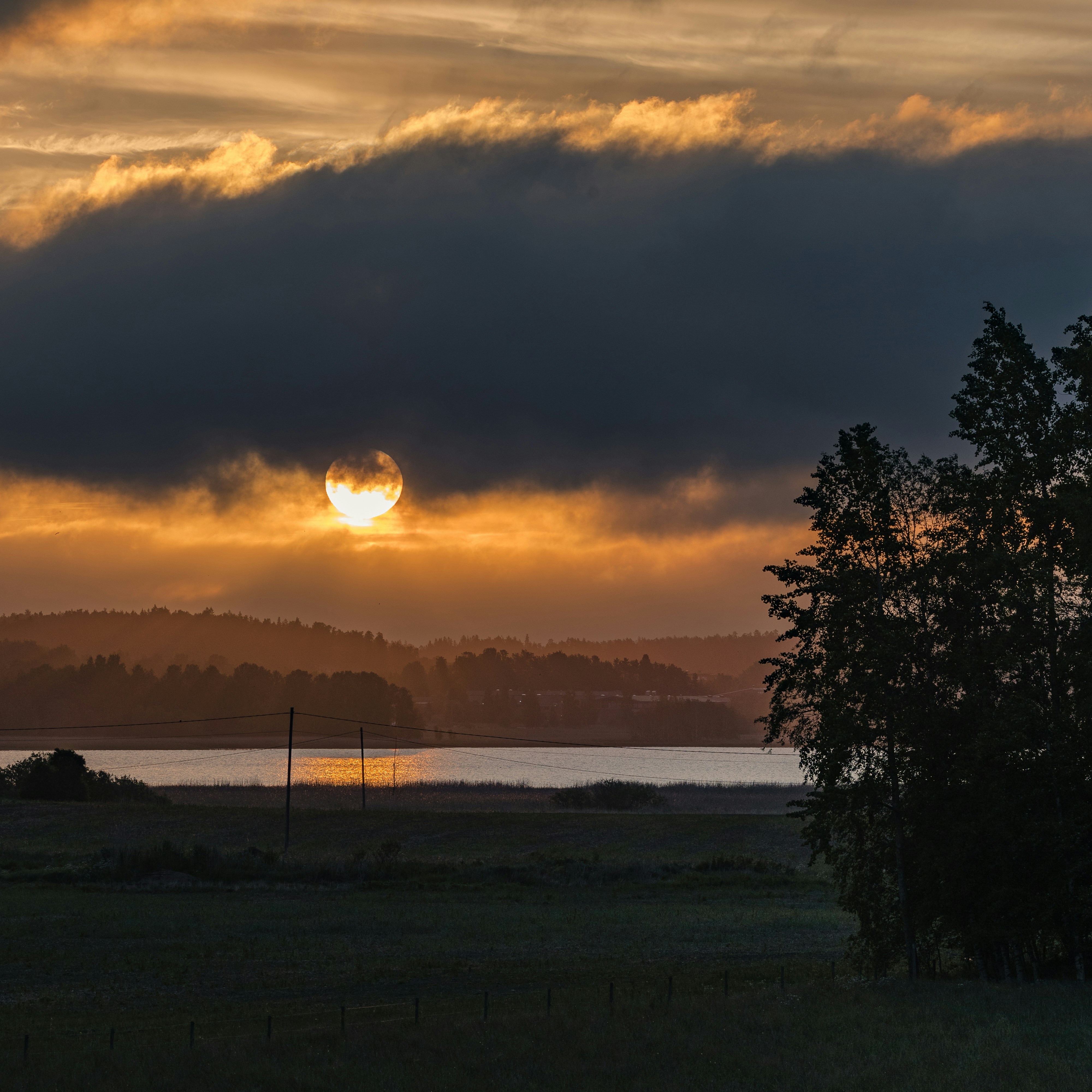 Golden sunset over a lake with dark clouds and trees.