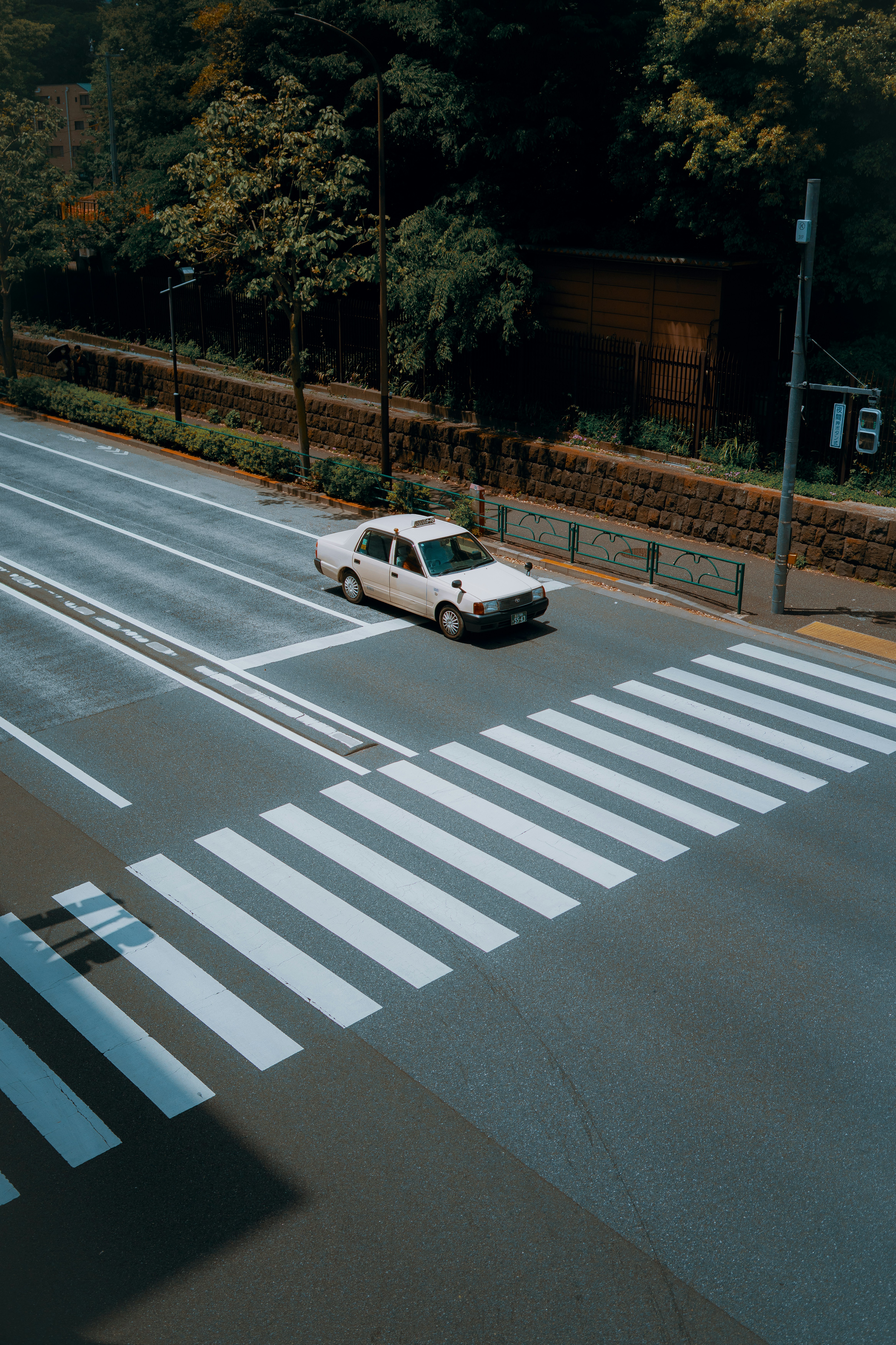 A white car drives on a road with a crosswalk.