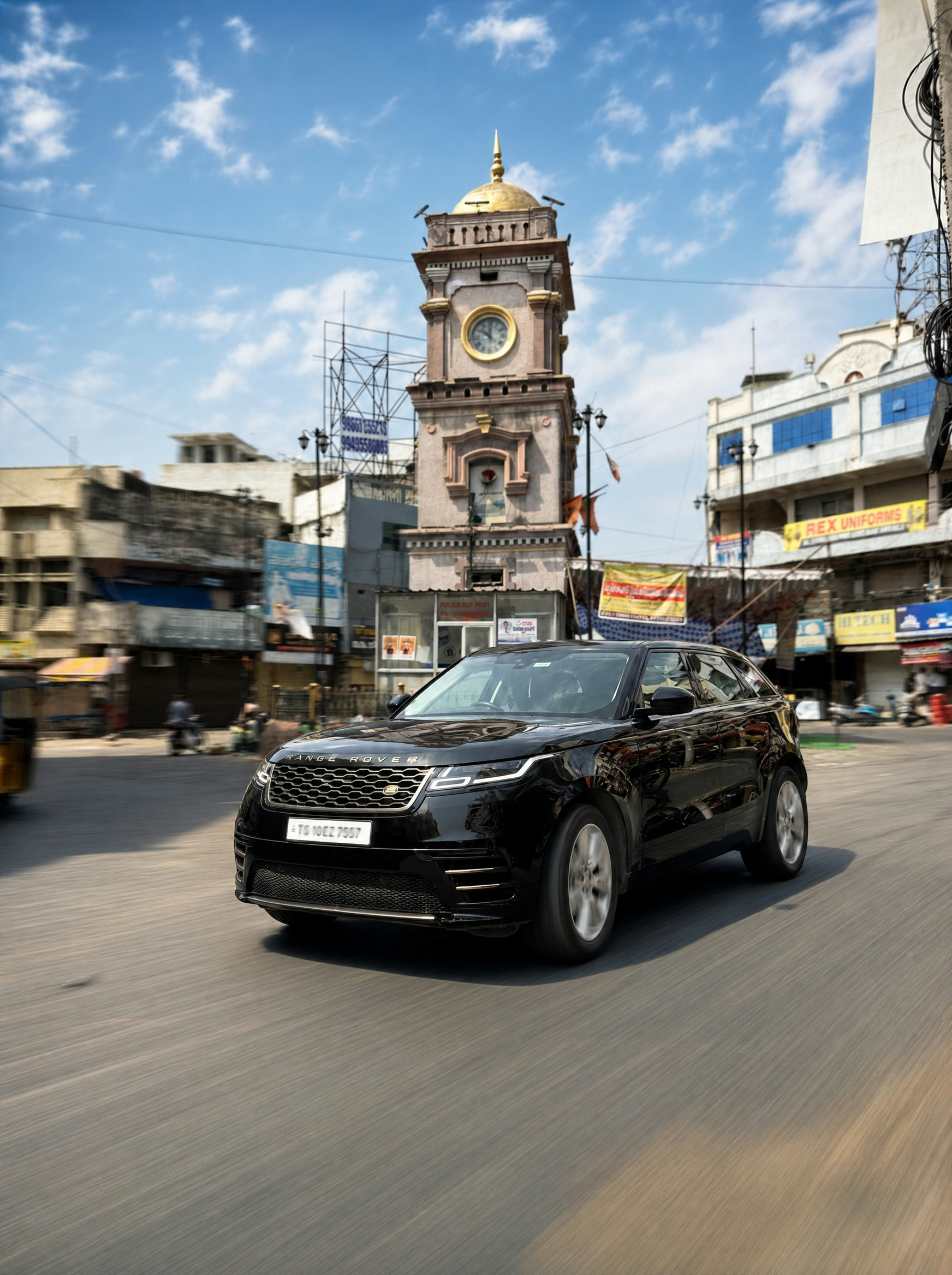 Black suv drives past an old clock tower.