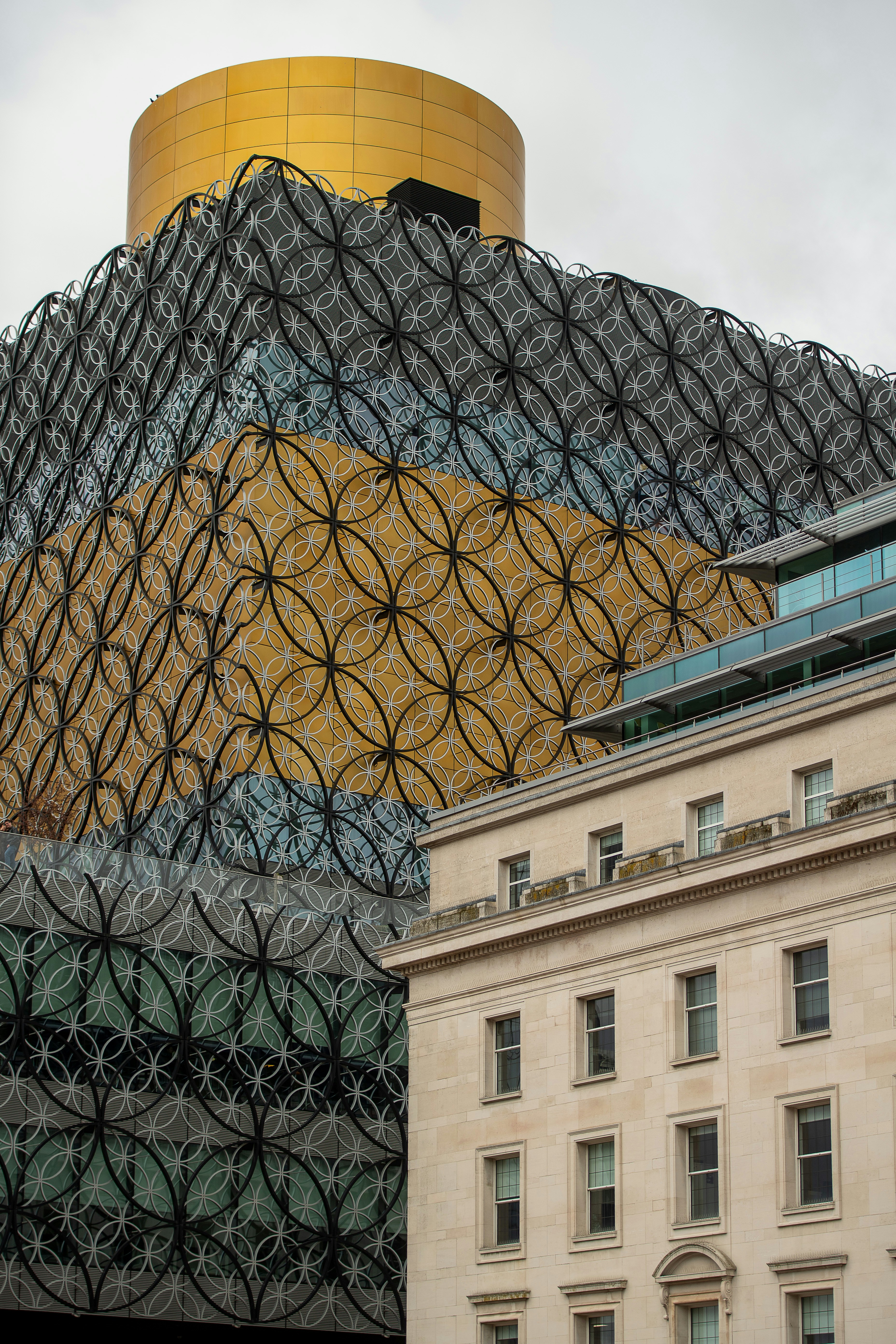 Modern patterned building with golden top next to classical architecture.