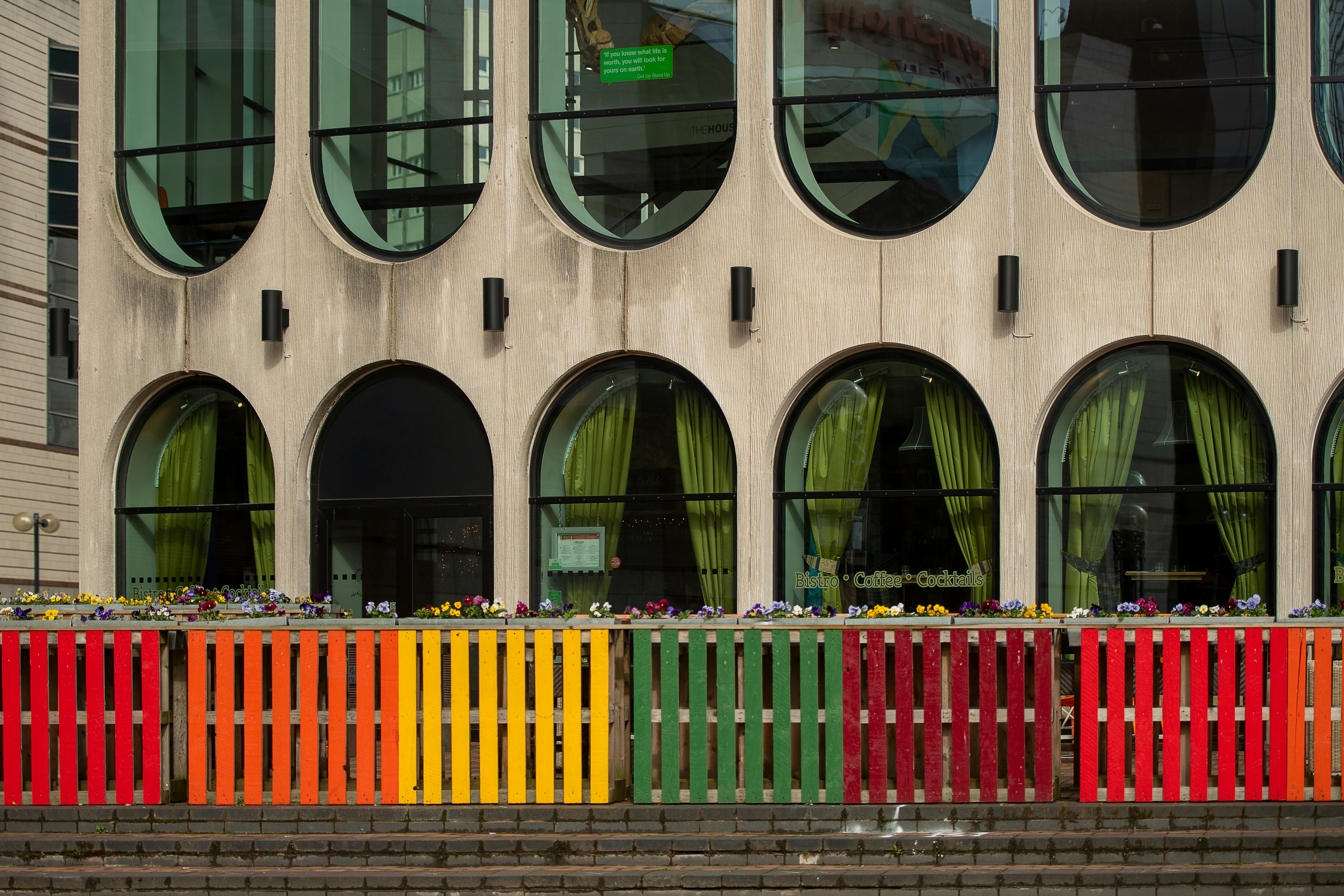 Vibrant rainbow pallets line a modern building's facade.