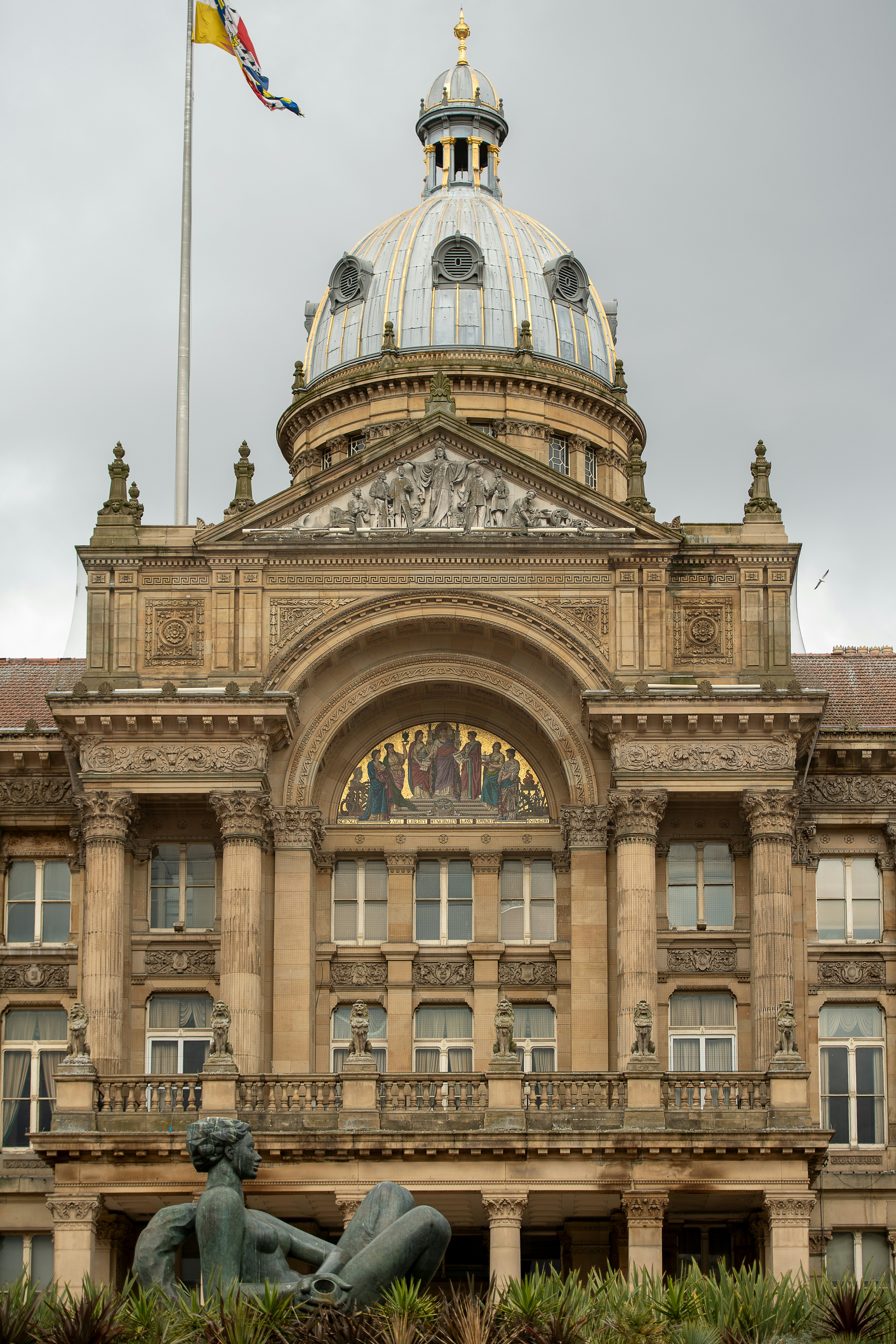 Grand ornate building with a dome, flag, and sculpture.