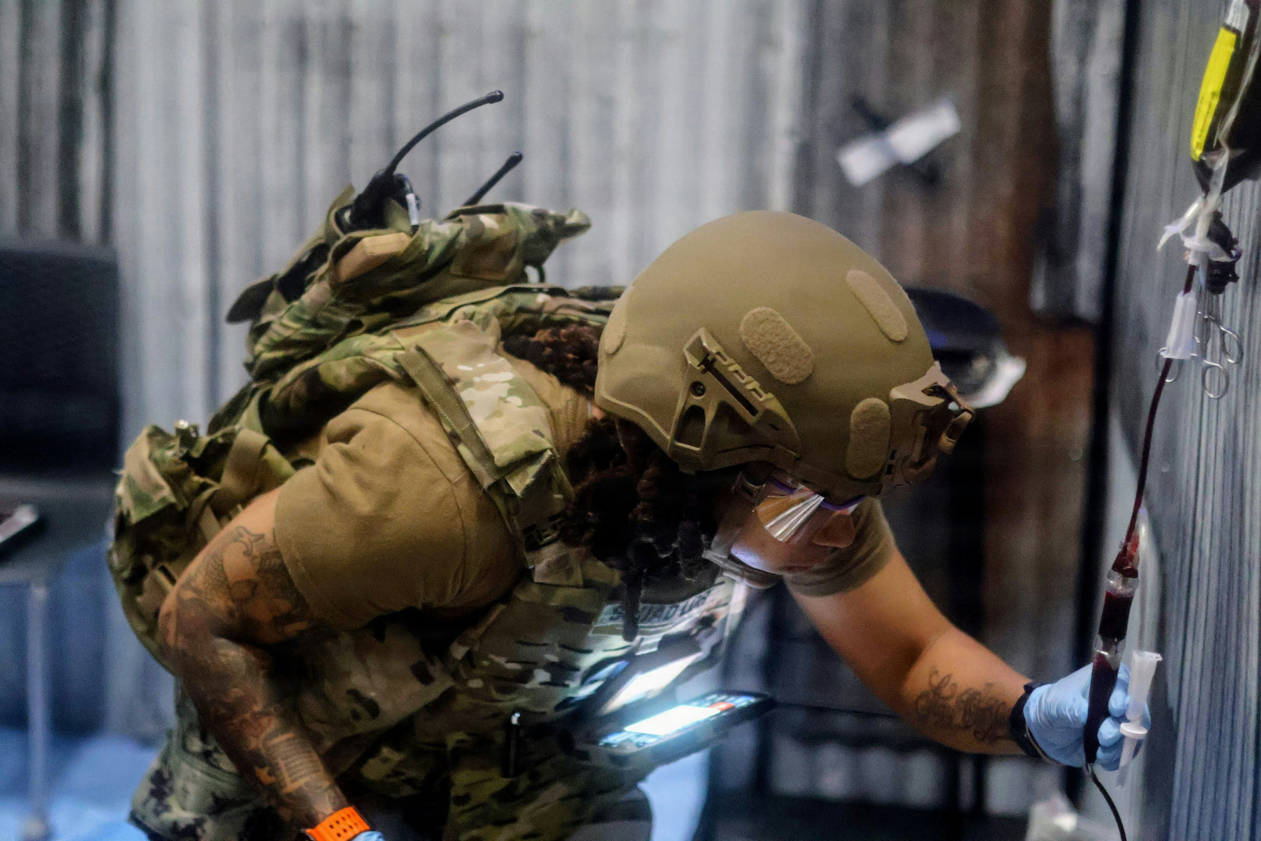 Soldier in tactical gear works with medical equipment.