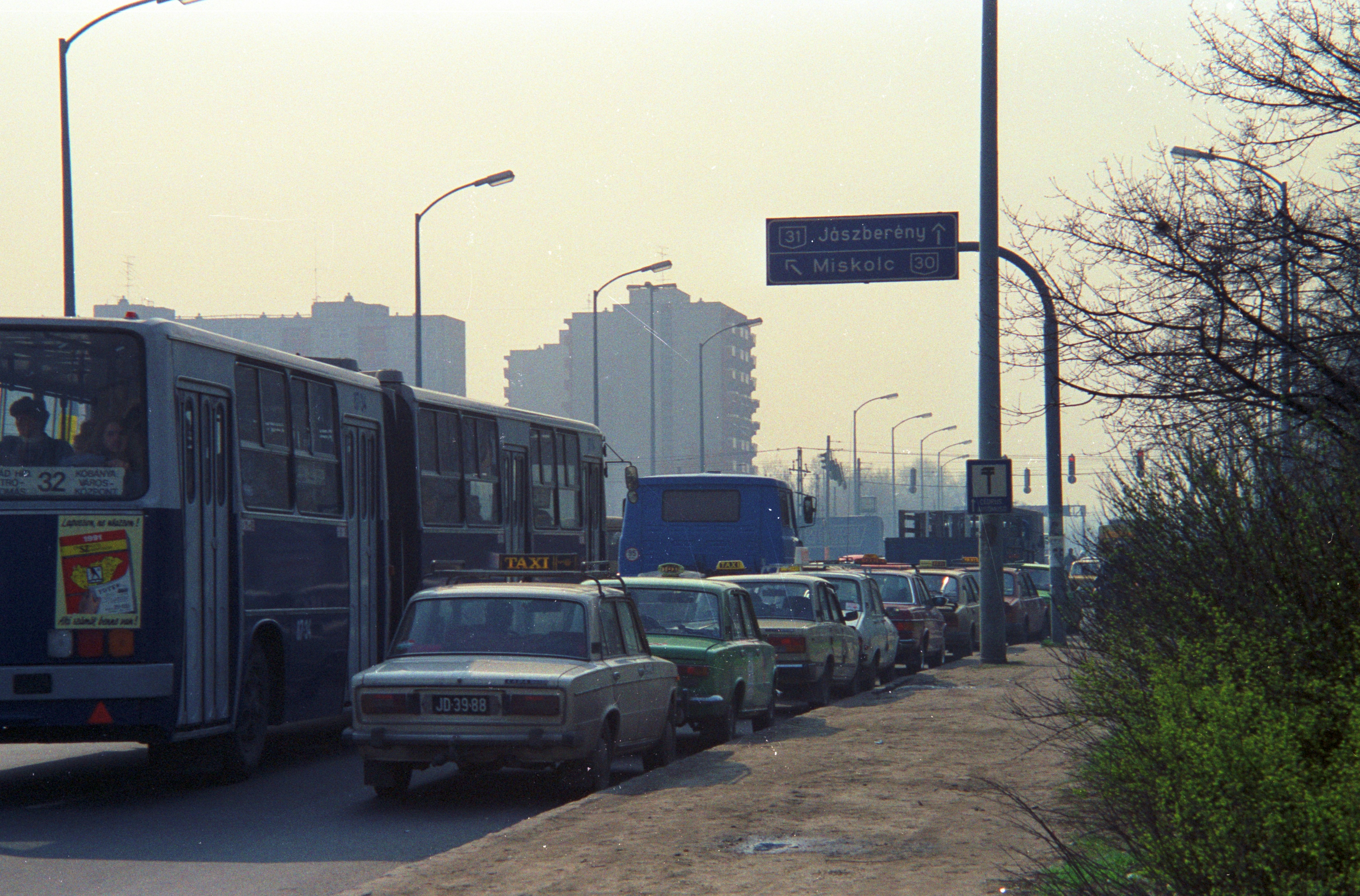 バスが市街地の道路に駐車中の車の横を通り過ぎます。