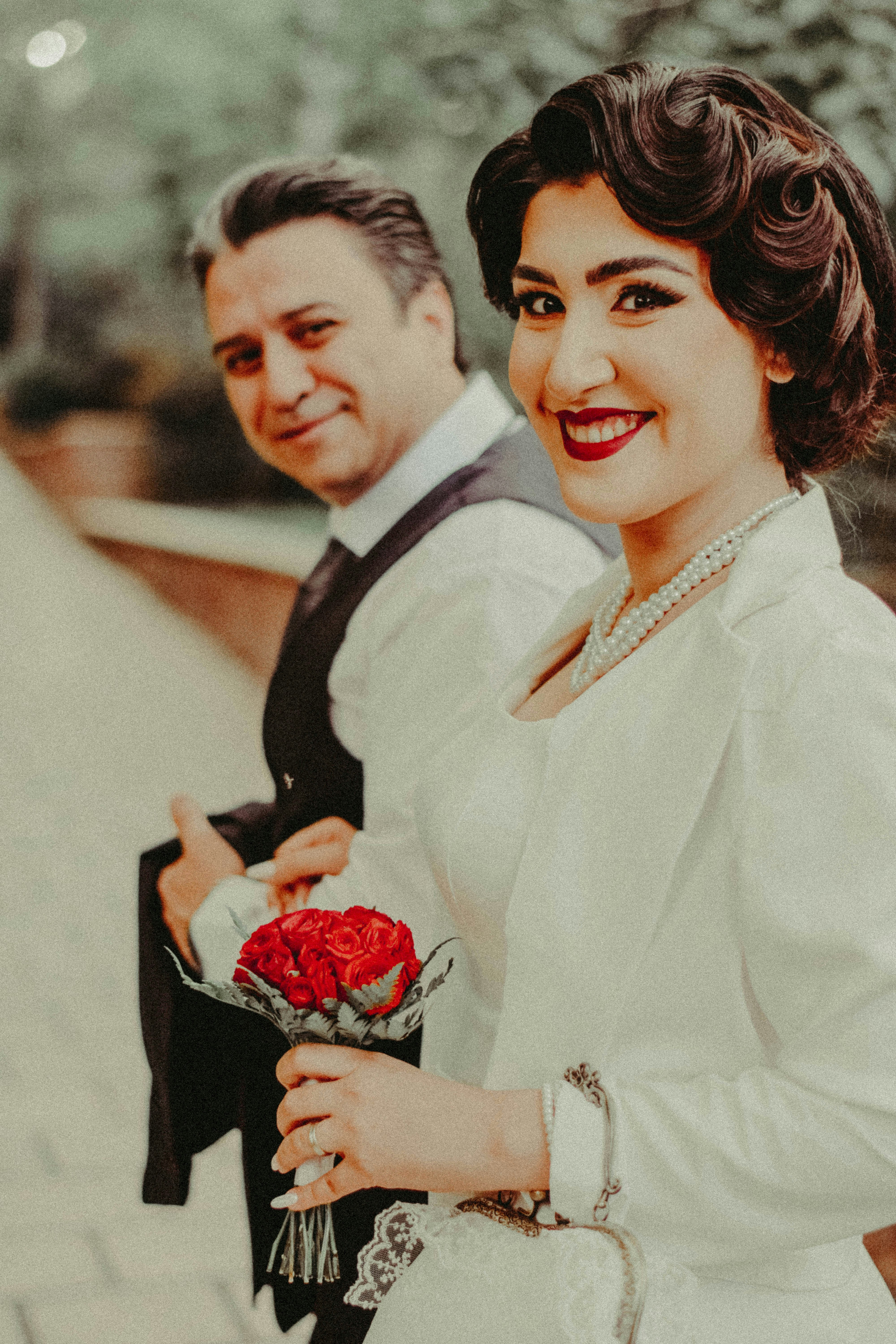 Smiling couple in vintage attire holding a red rose bouquet