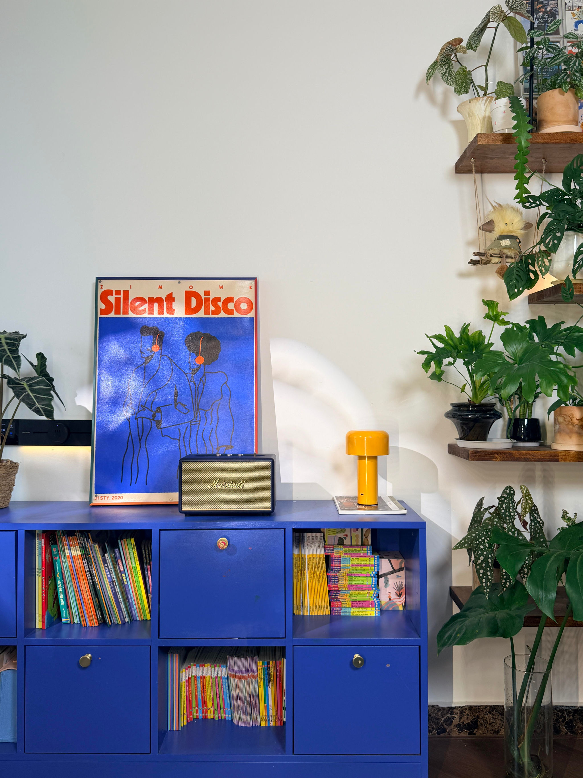 Cabinet bleu, affiche « silent disco », haut-parleur, lampe et plantes.