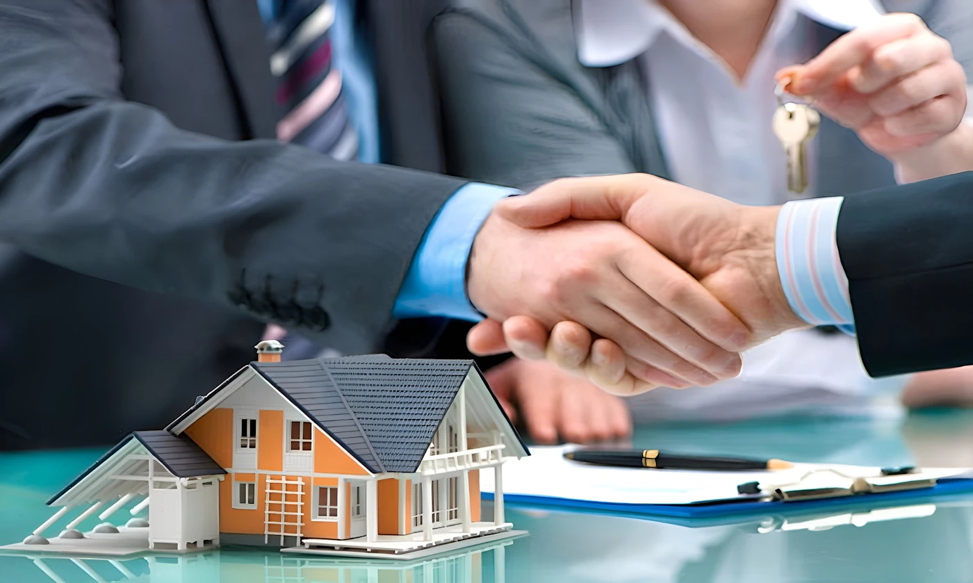 An agent and a homebuyer shaking hands over a house model and keys