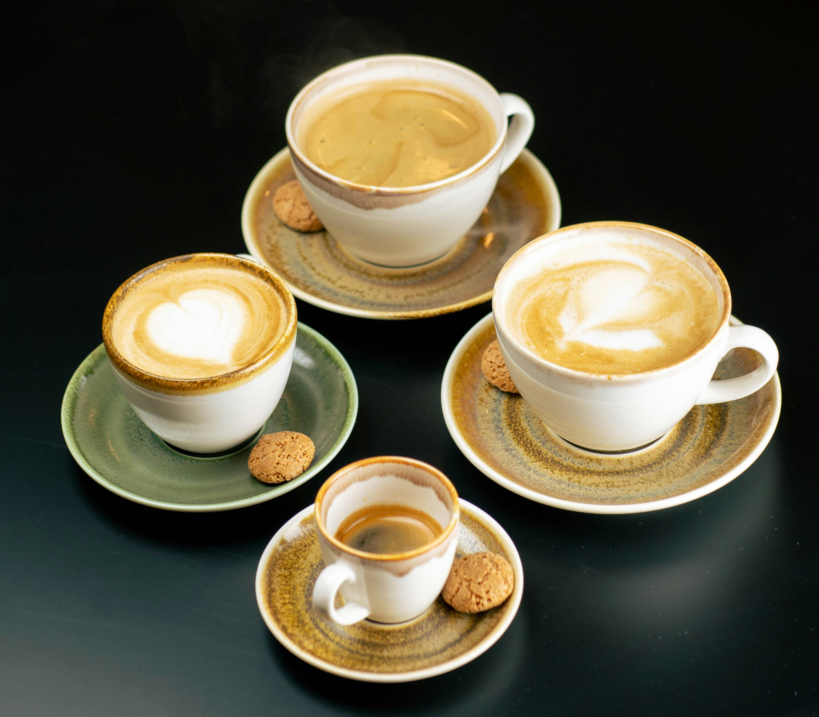 Four cups of coffee with cookies on a dark background.