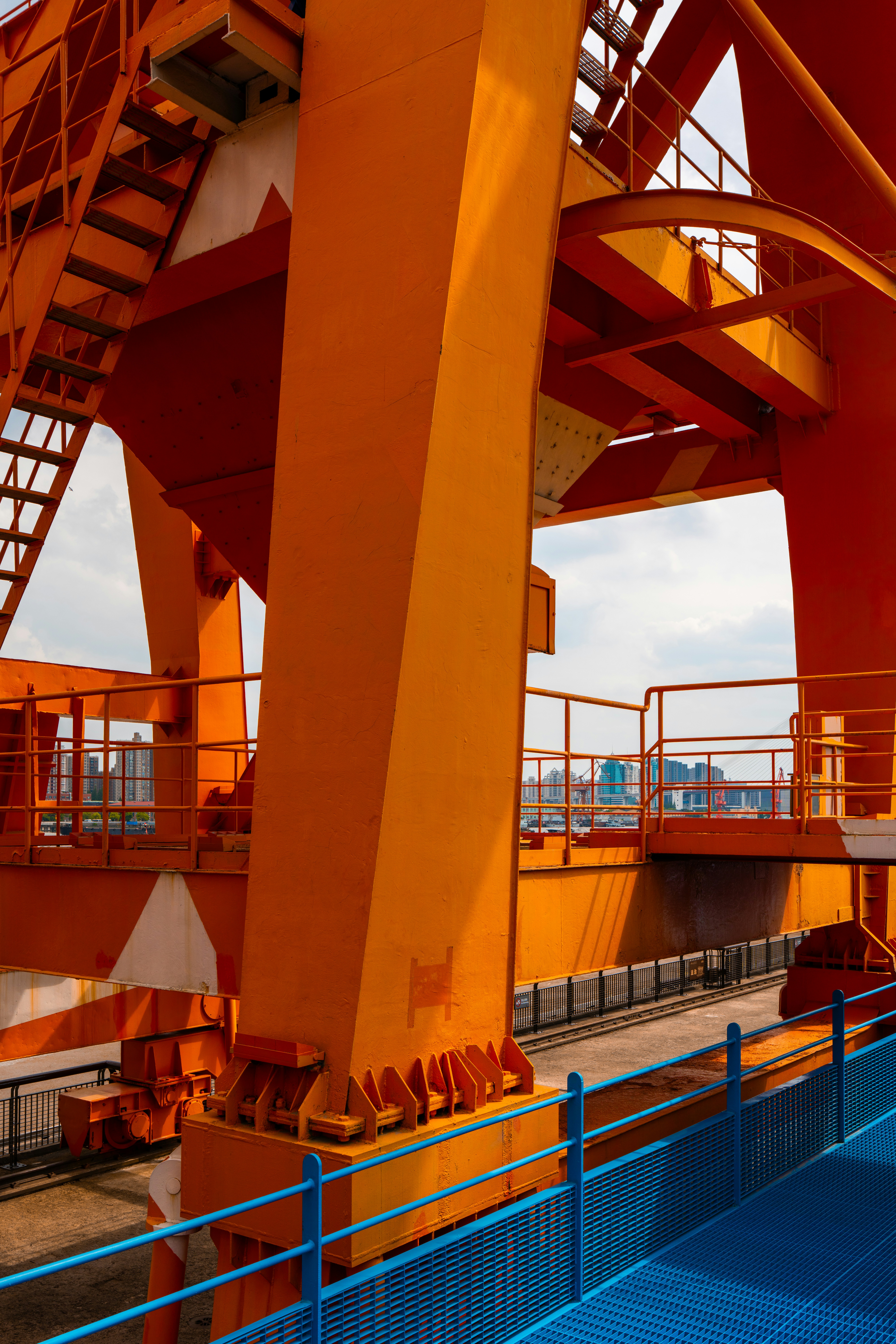 Una vivace struttura arancione di gru industriale contro lo skyline di una città.