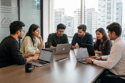 Six colleagues collaborating around a conference table with laptops.