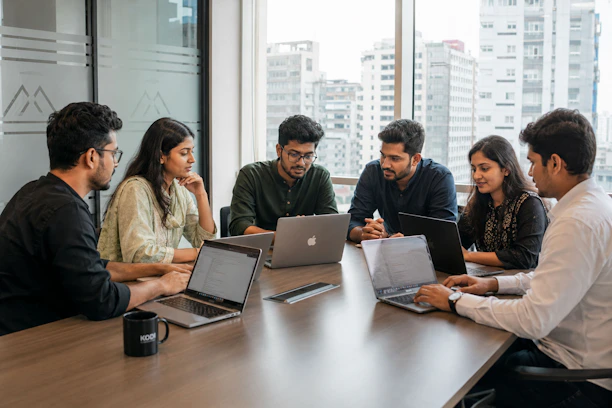 Six colleagues collaborating around a conference table with laptops.