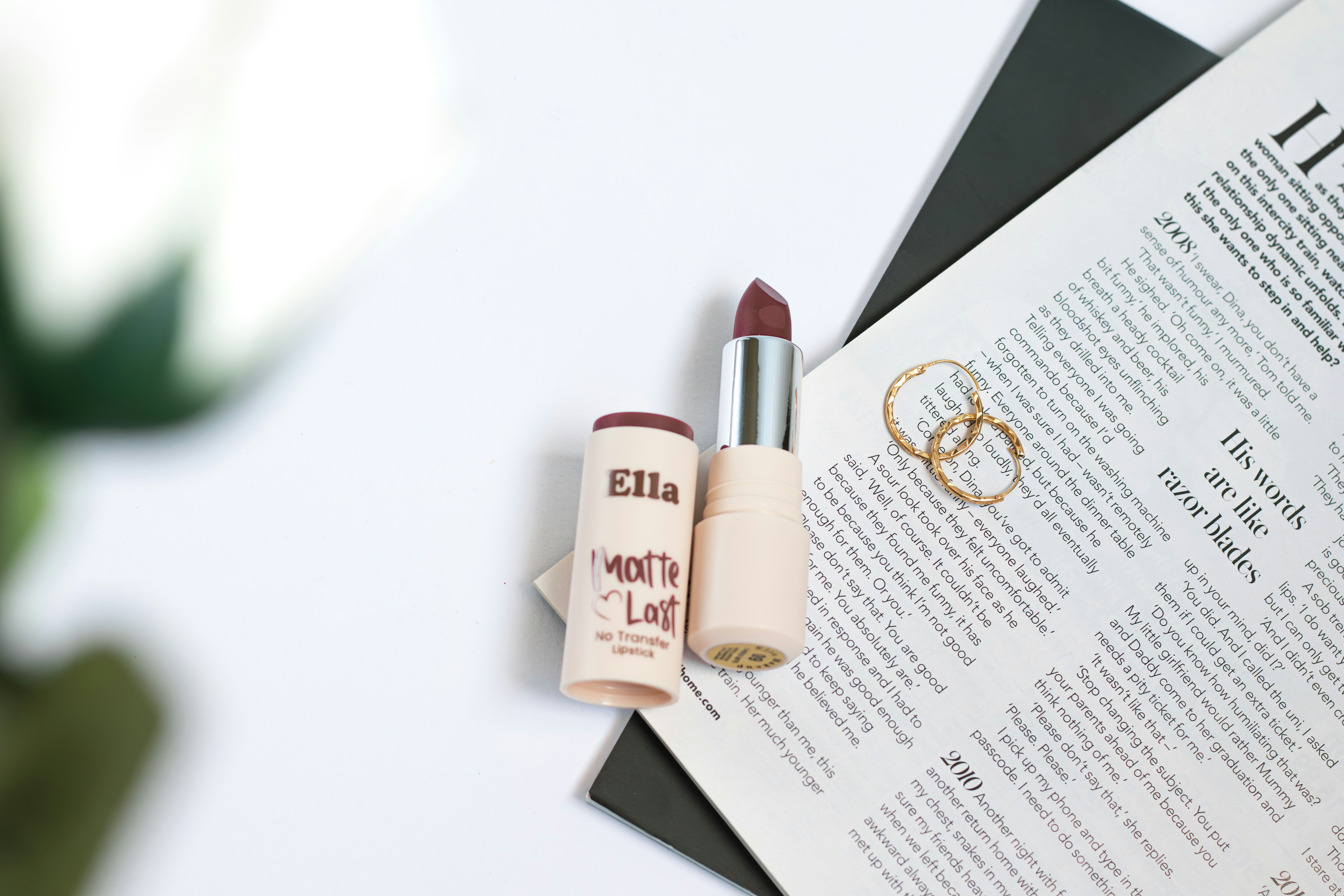 Dark red lipstick, gold rings, and newspaper on white surface.