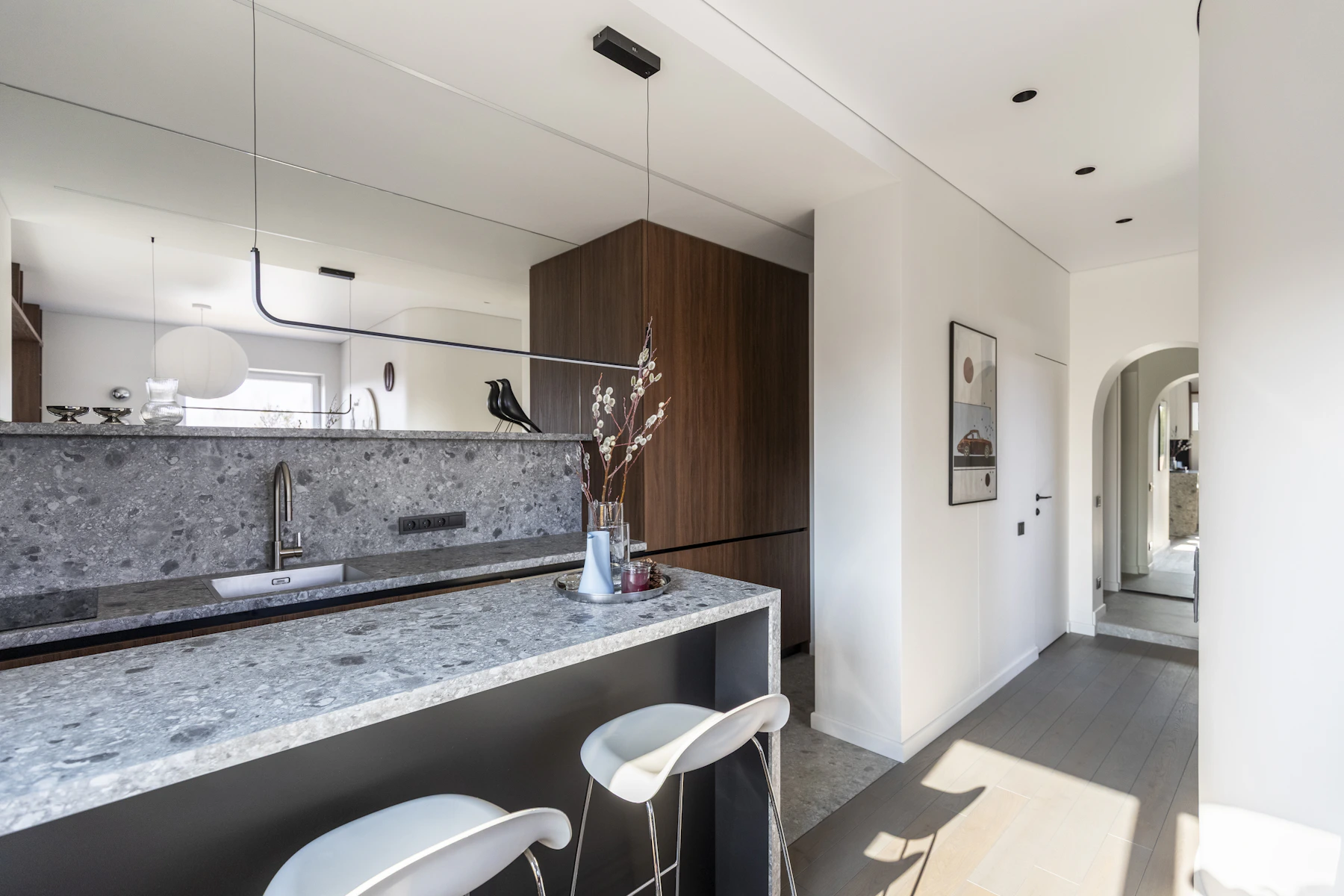 Compact kitchen with speckled counters, dark wood tall cabinetry, white stools and a long globe light