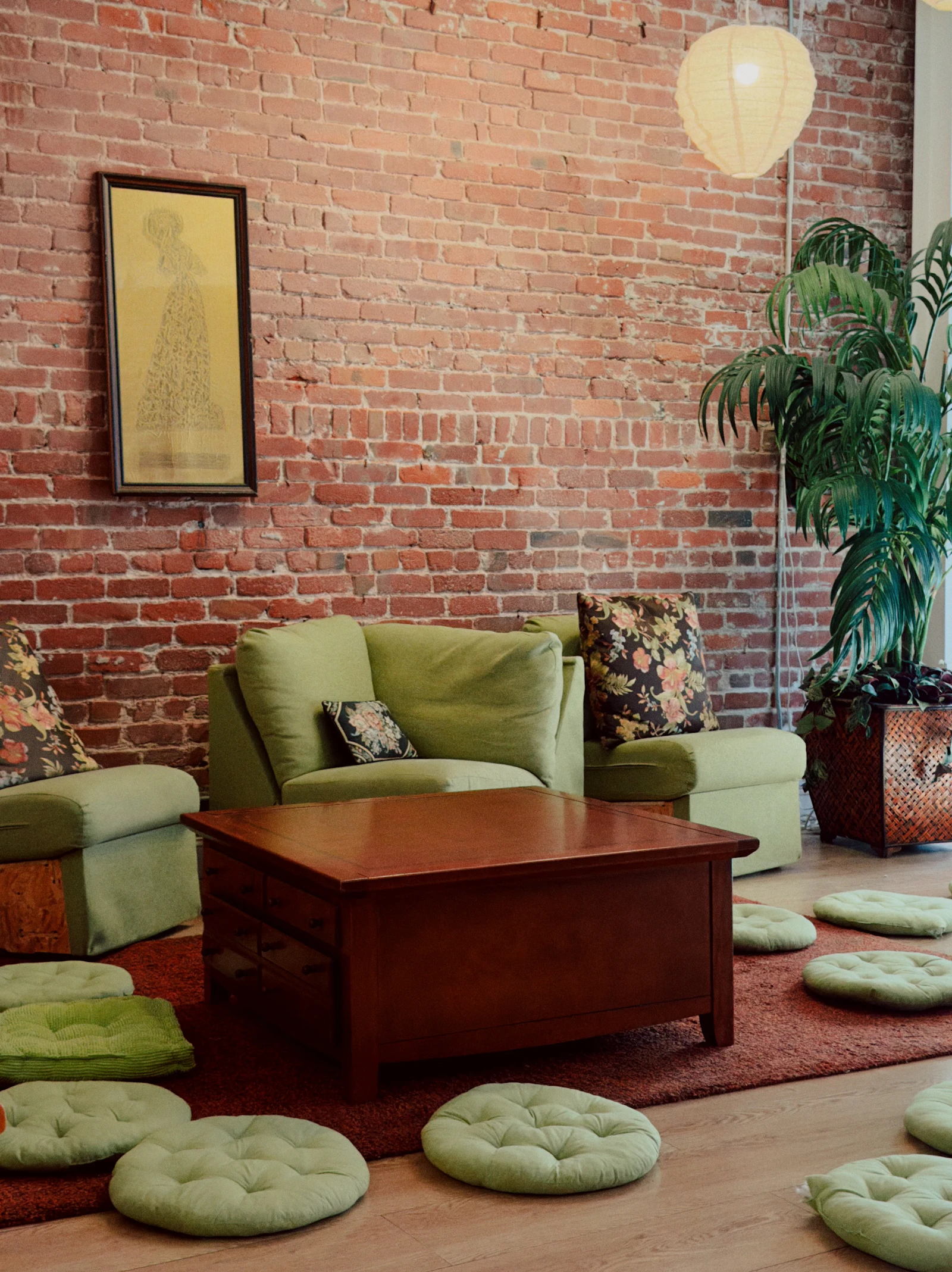 A room with a brick wall, green furniture and floor cushions