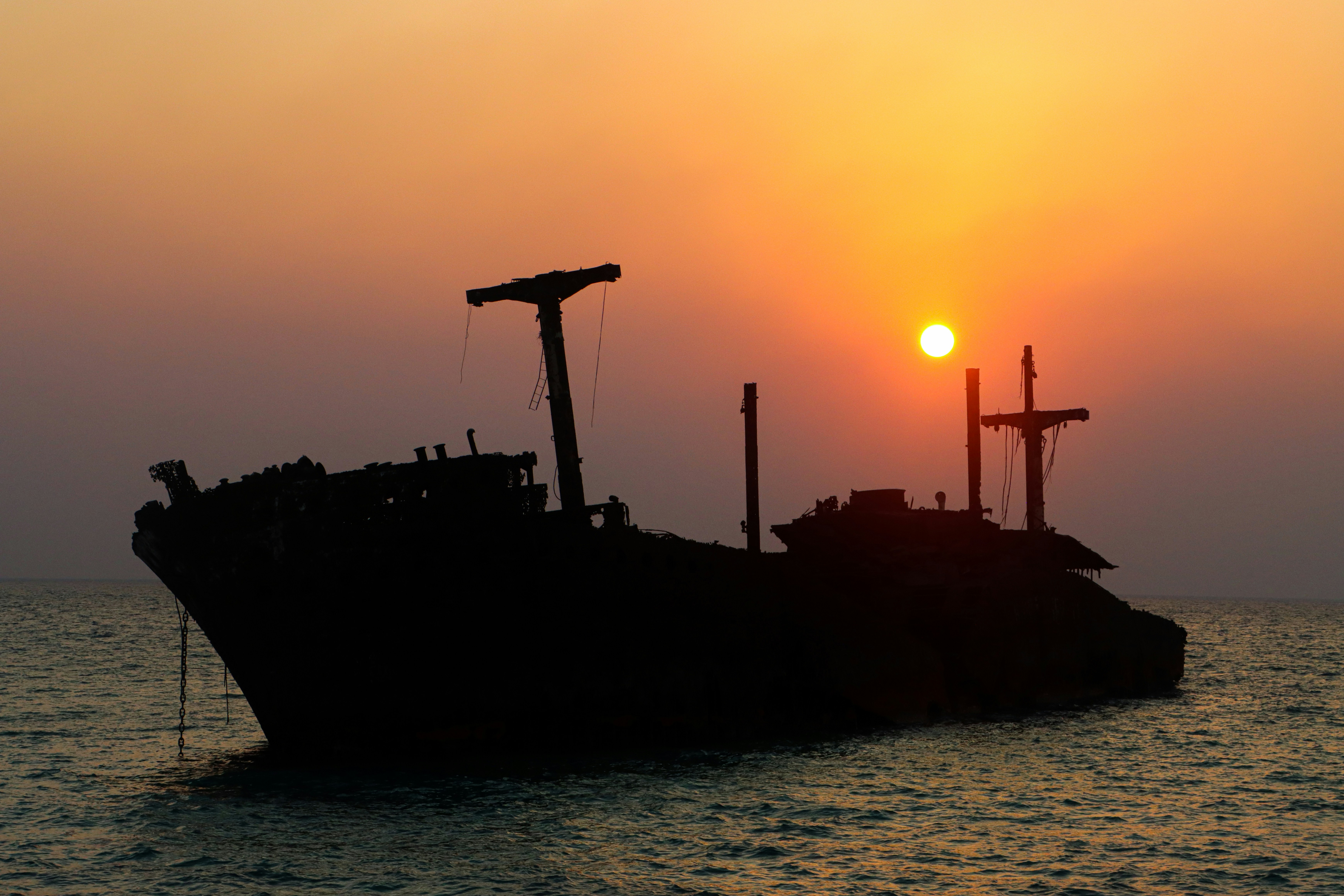 A shipwreck silhouetted against a vibrant sunset over the ocean