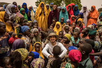 A man smiles surrounded by many happy children and women.