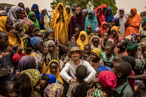A man smiles surrounded by many happy children and women.