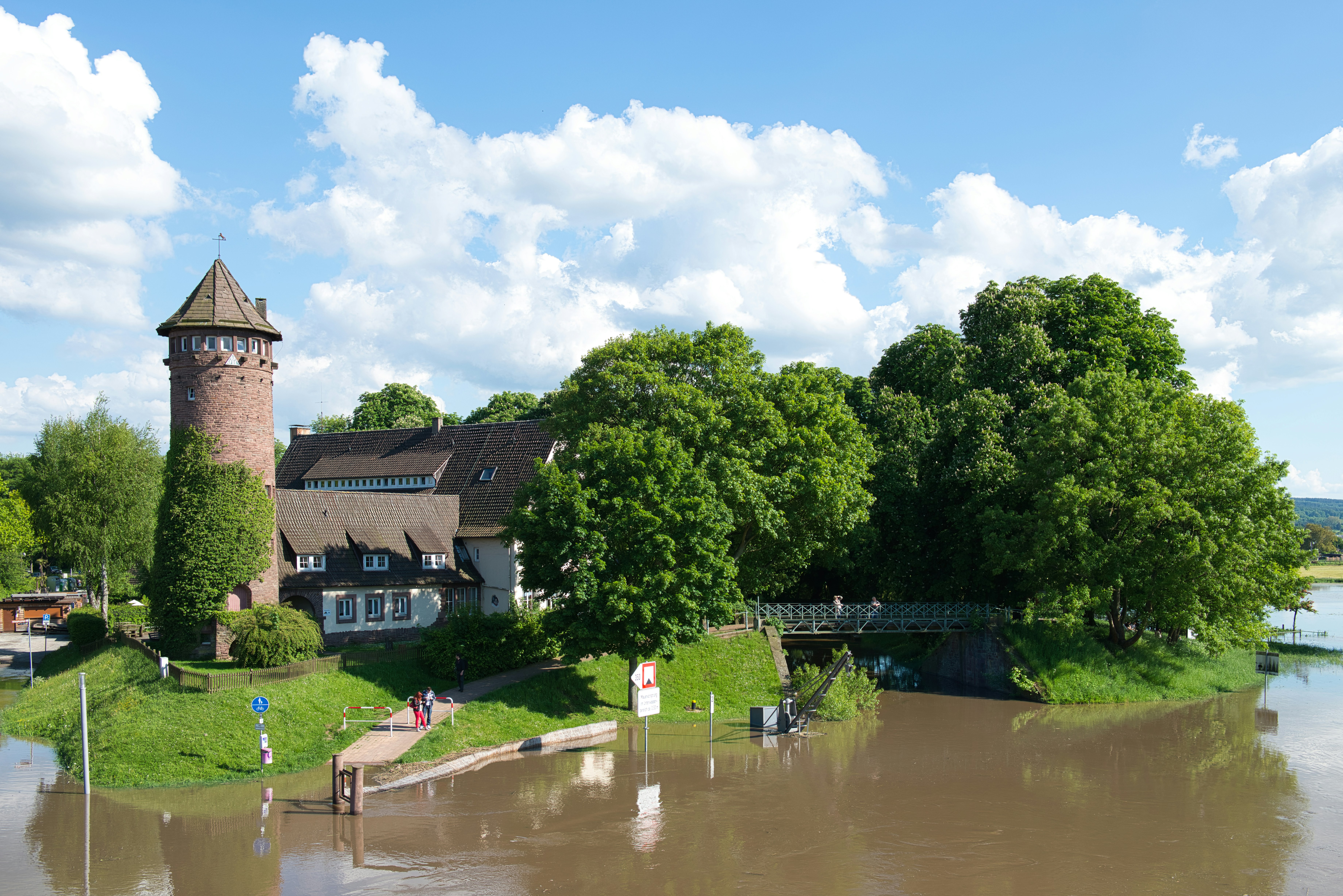 Medieval-style tower and lush trees by a brown river.