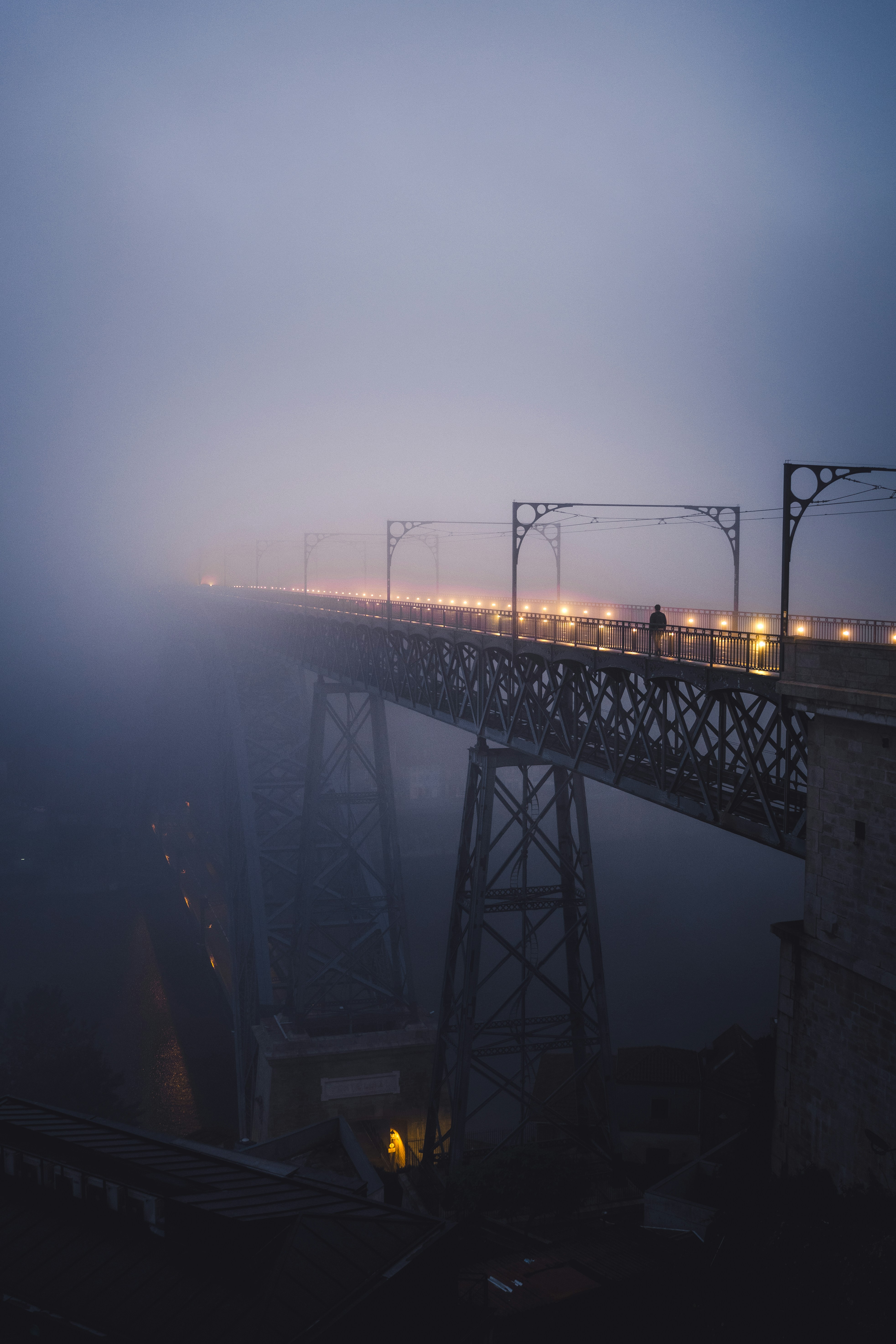 A person walks on a foggy, illuminated bridge at dusk.