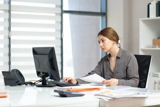 Young woman focused on computer and documents at office desk.