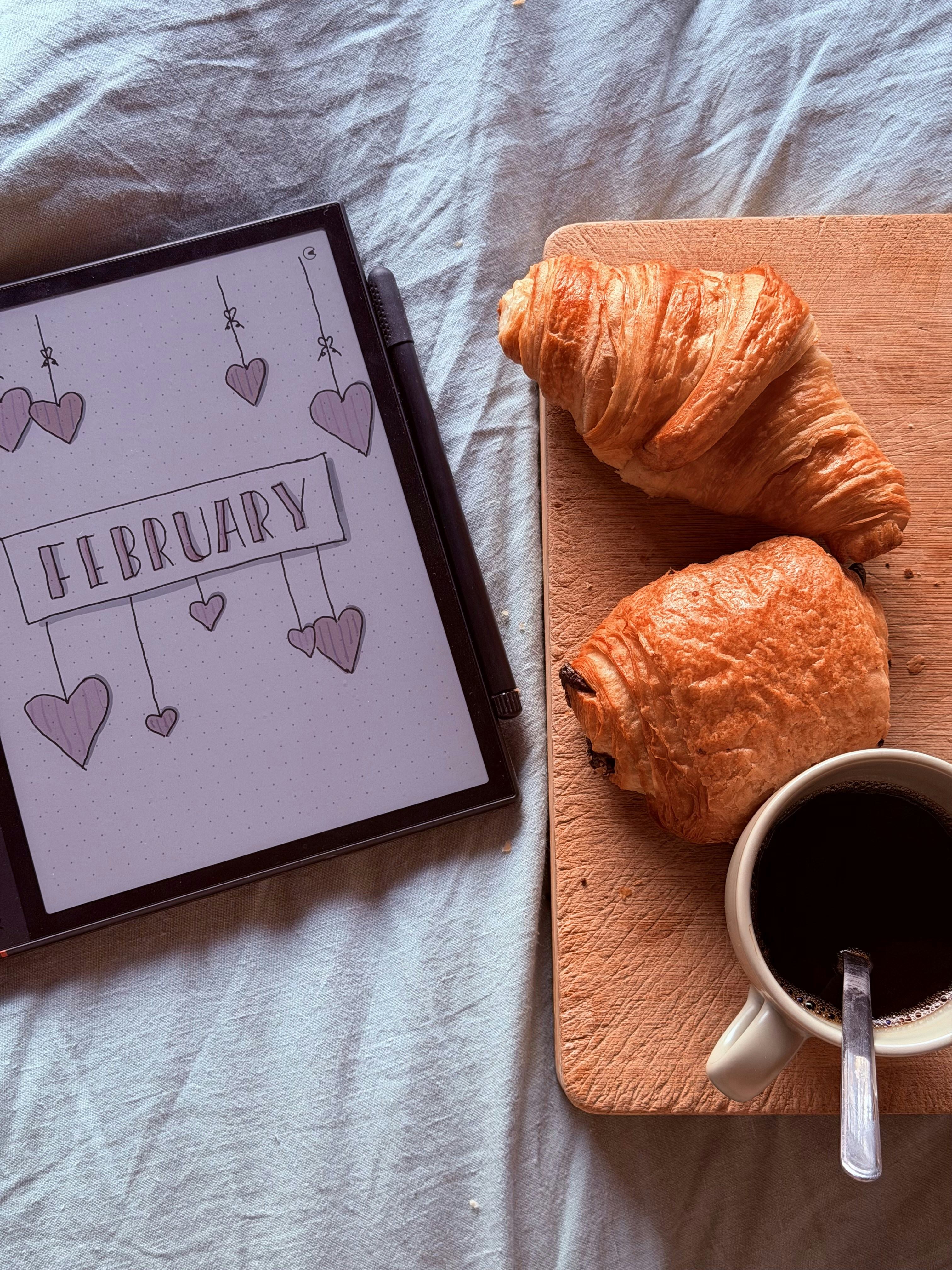 Tablet with "february" and pastries with coffee on a bed.