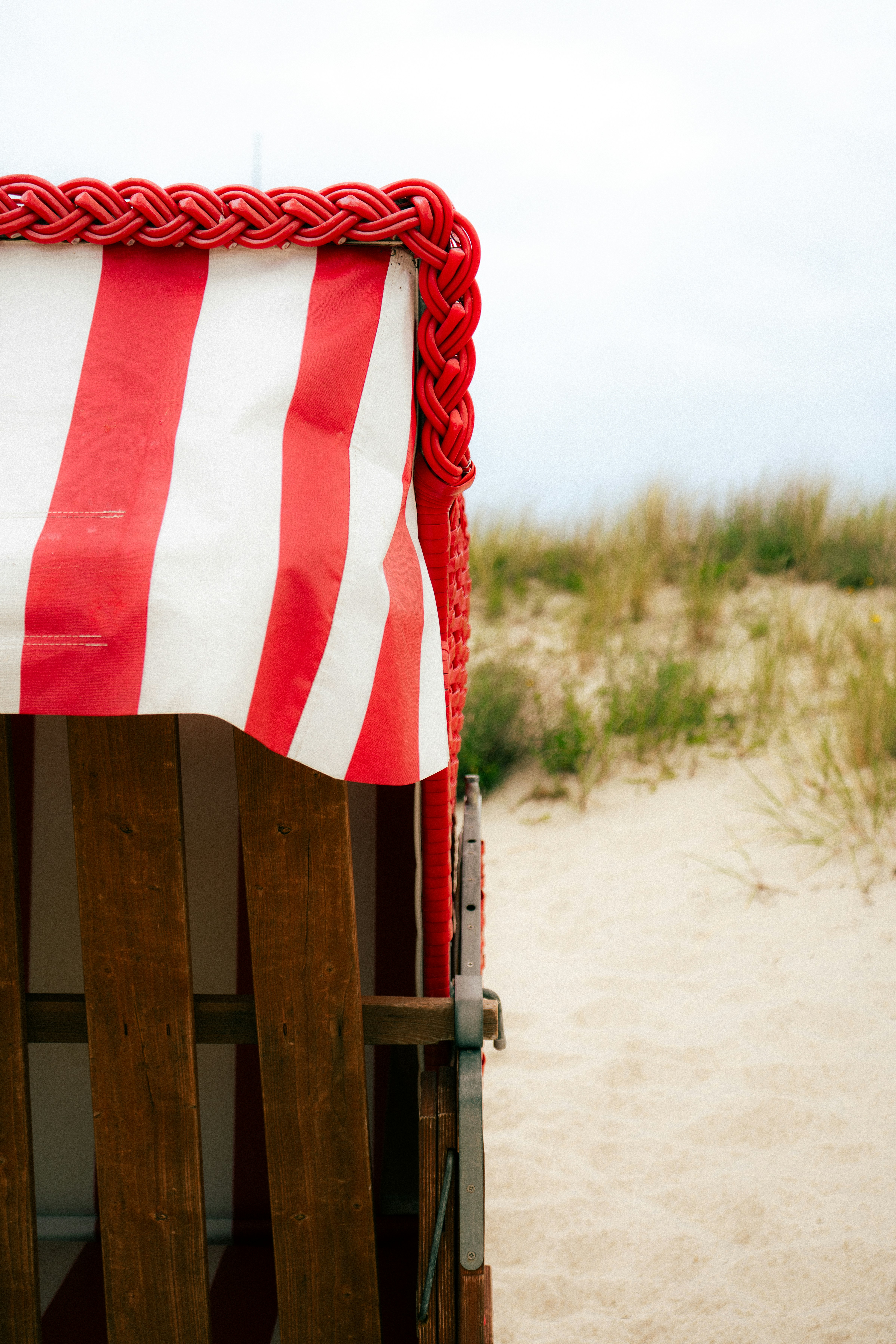 Une chaise longue de plage rayée rouge et blanche près de dunes de sable.
