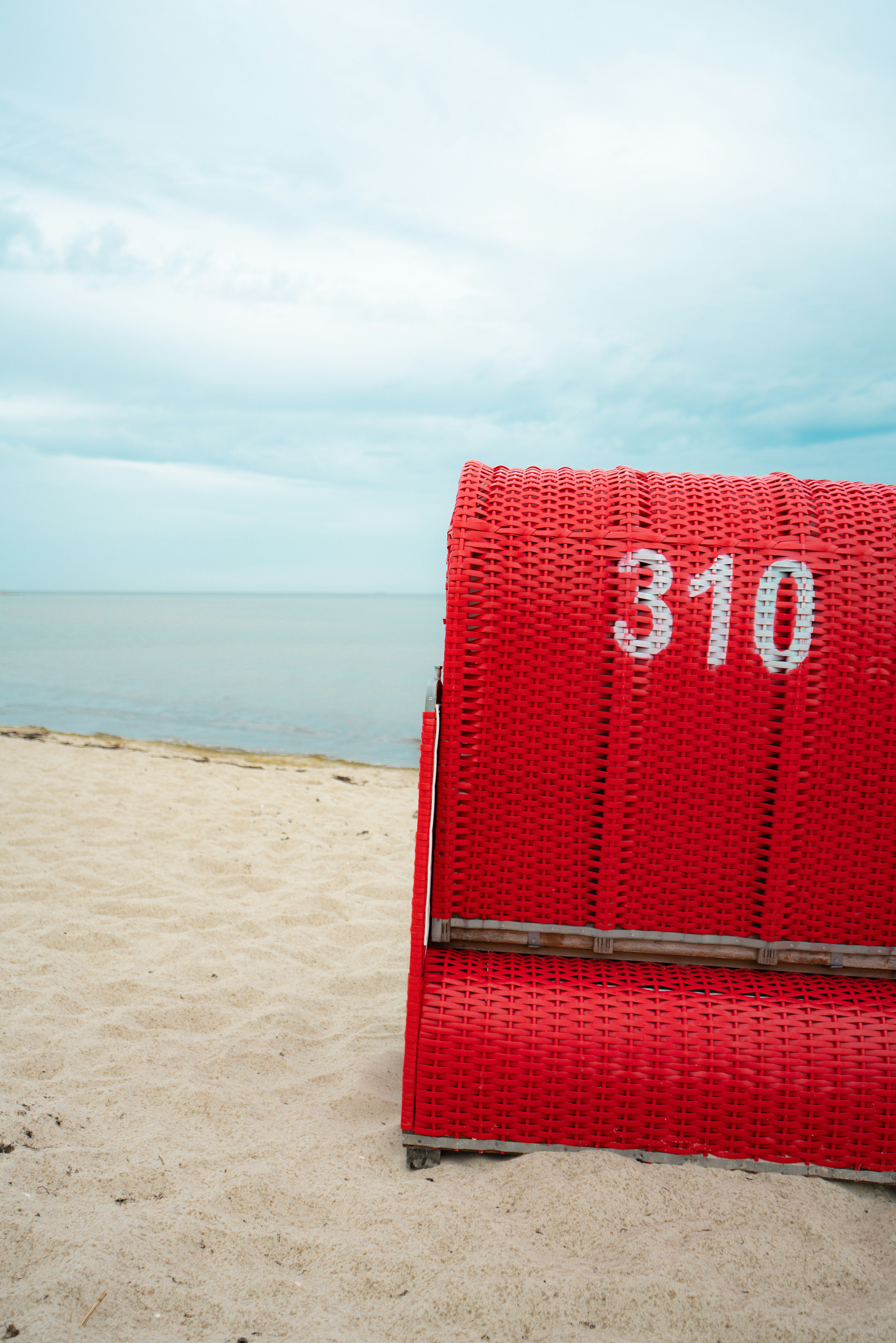 Chaise longue rouge 310 sur une plage de sable.