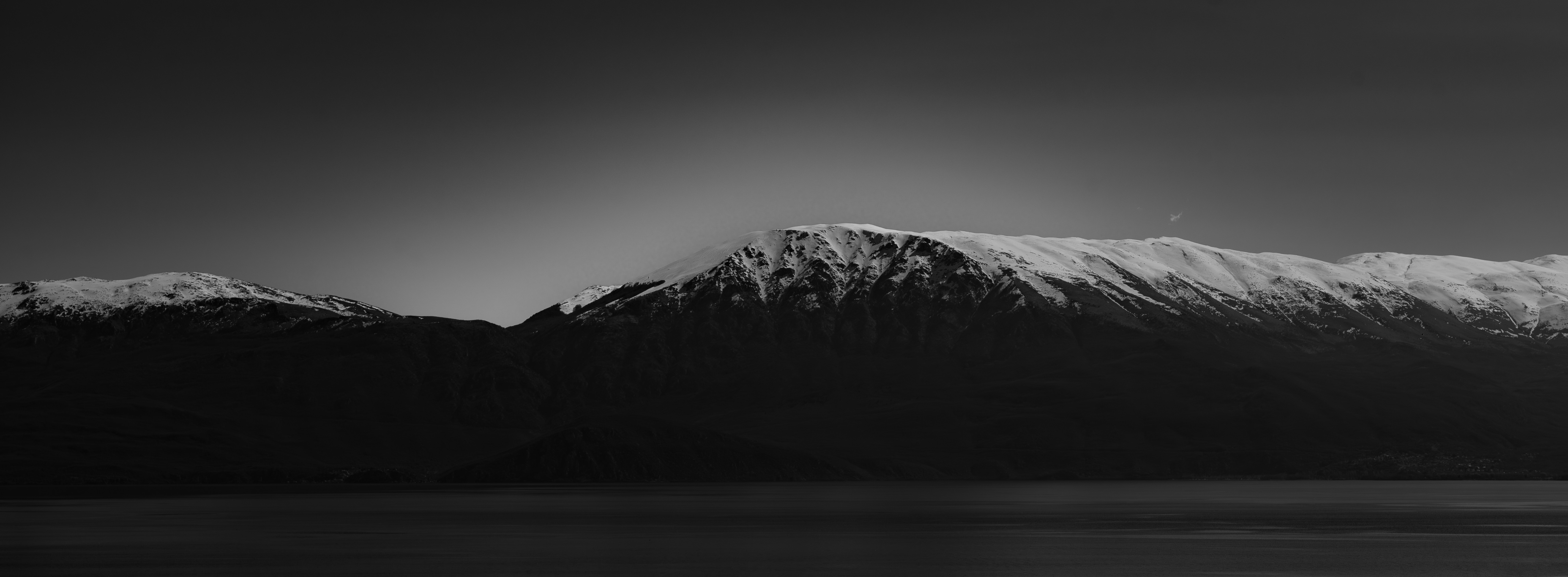 Paesaggio monocromatico con montagne innevate e acqua scura.
