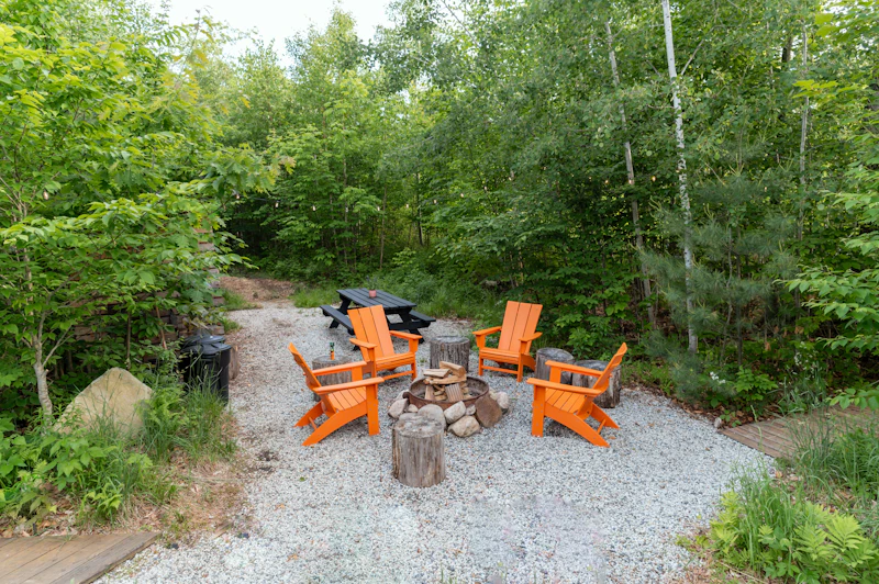 Gravel fire pit circle with orange chairs set inside a wooded garden