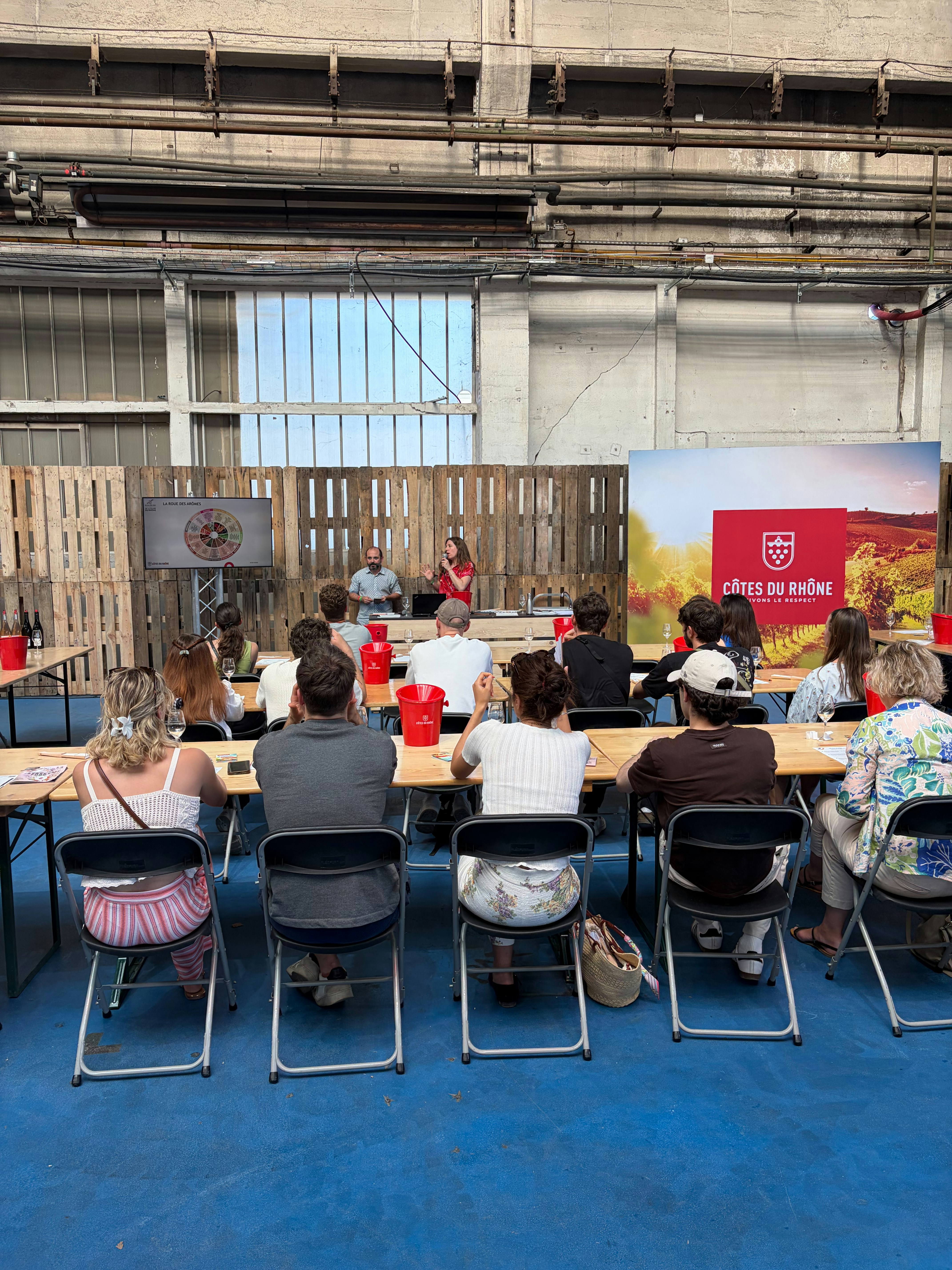 Masterclass devant un stand Côtes du Rhône orné d'un décor de vignes, le public attablé dans la halle du festival