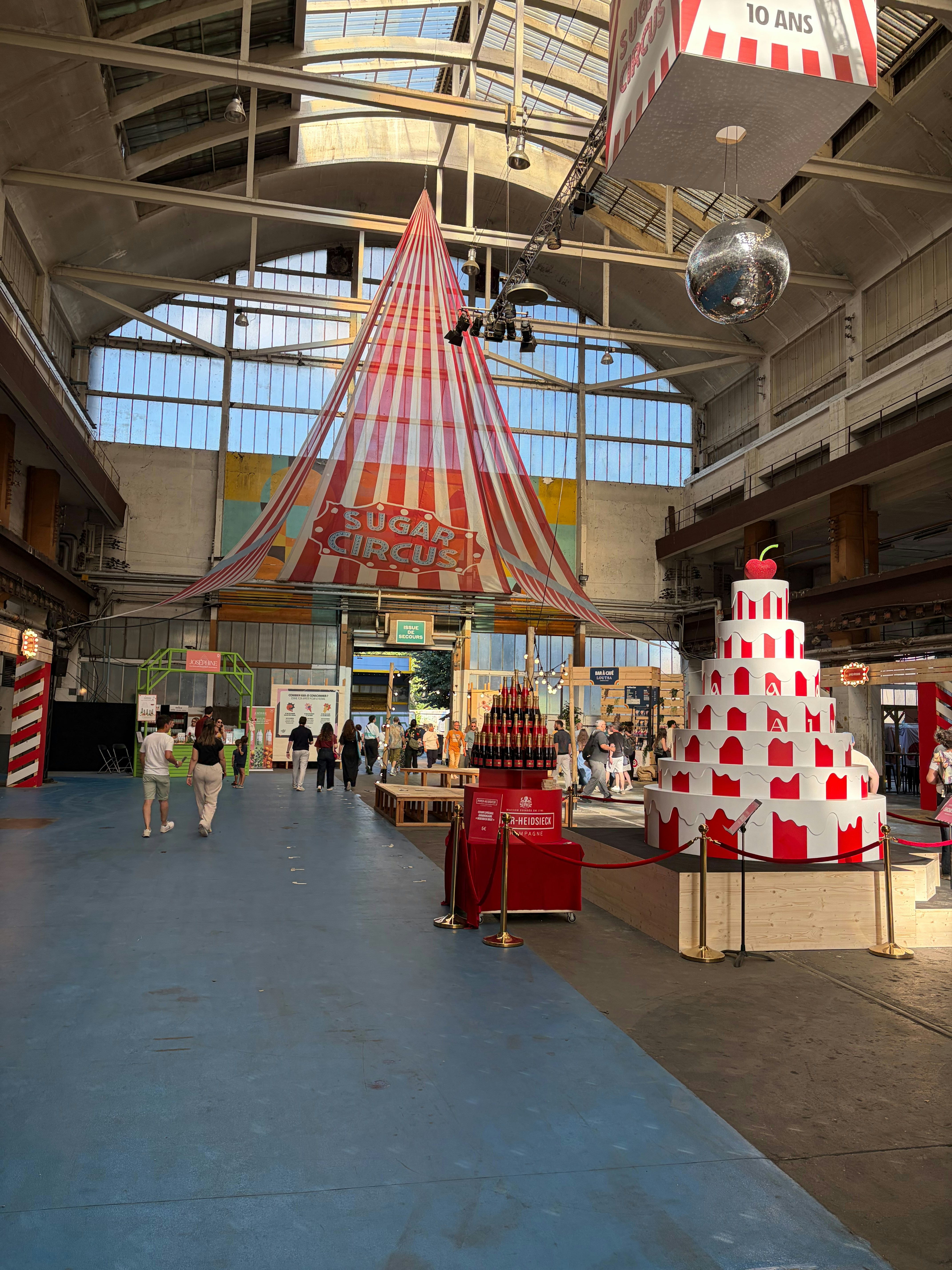 Grande halle des Grandes Locos avec un chapiteau rayé et une pièce montée géante rouge et blanc, pour les dix ans du Lyon Street Food Festival