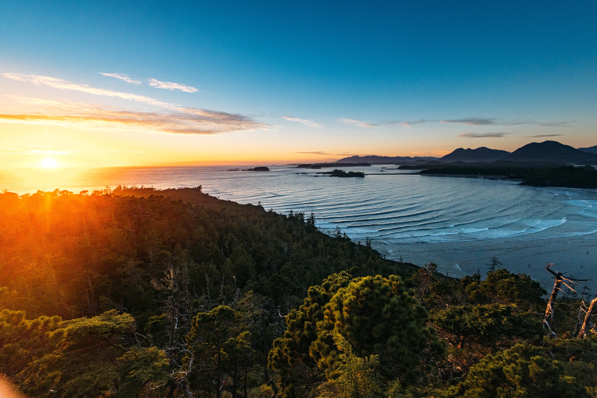 Golden sunset over a vast ocean with forested islands.