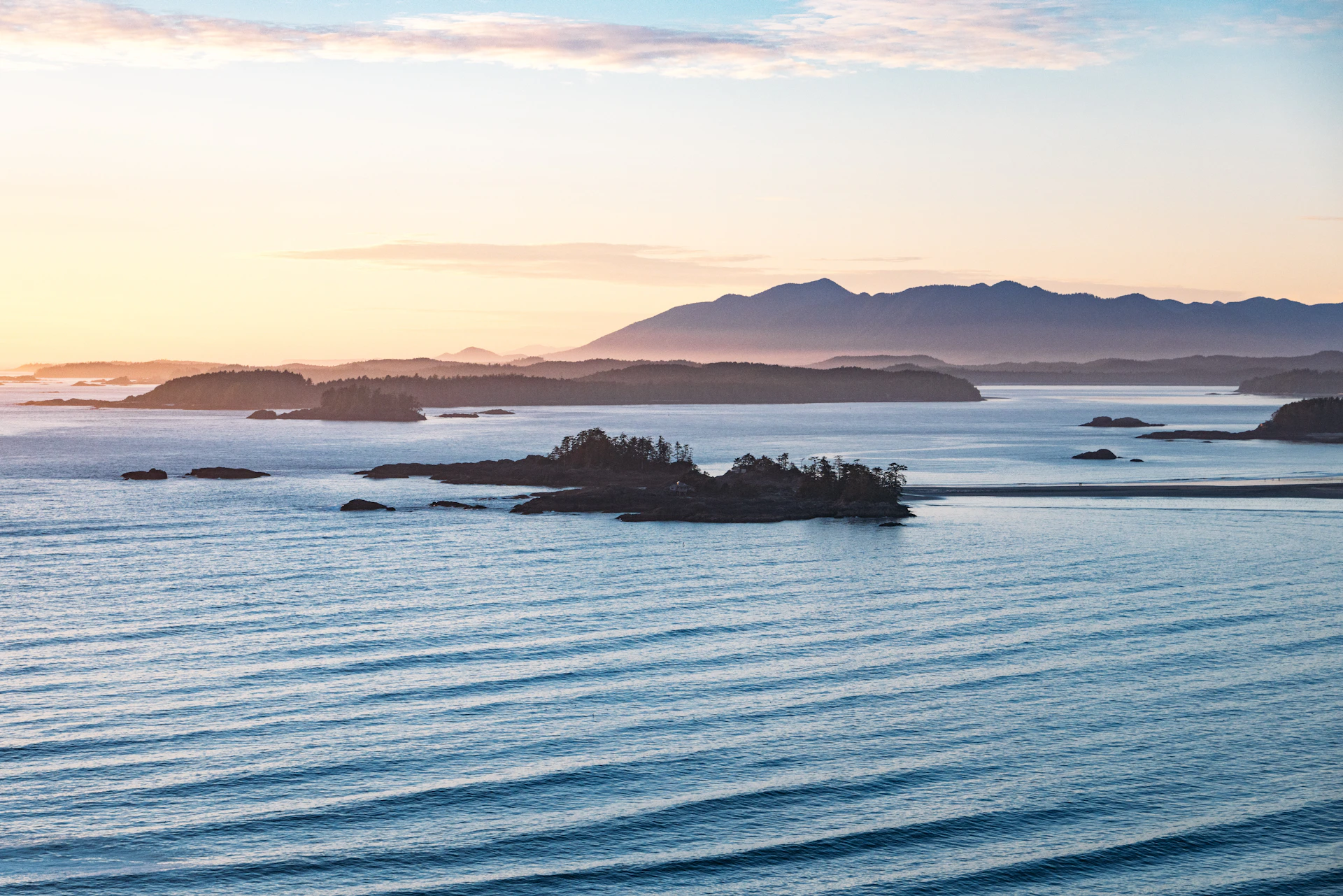 Ocean waves, small islands, and distant mountains at sunrise.