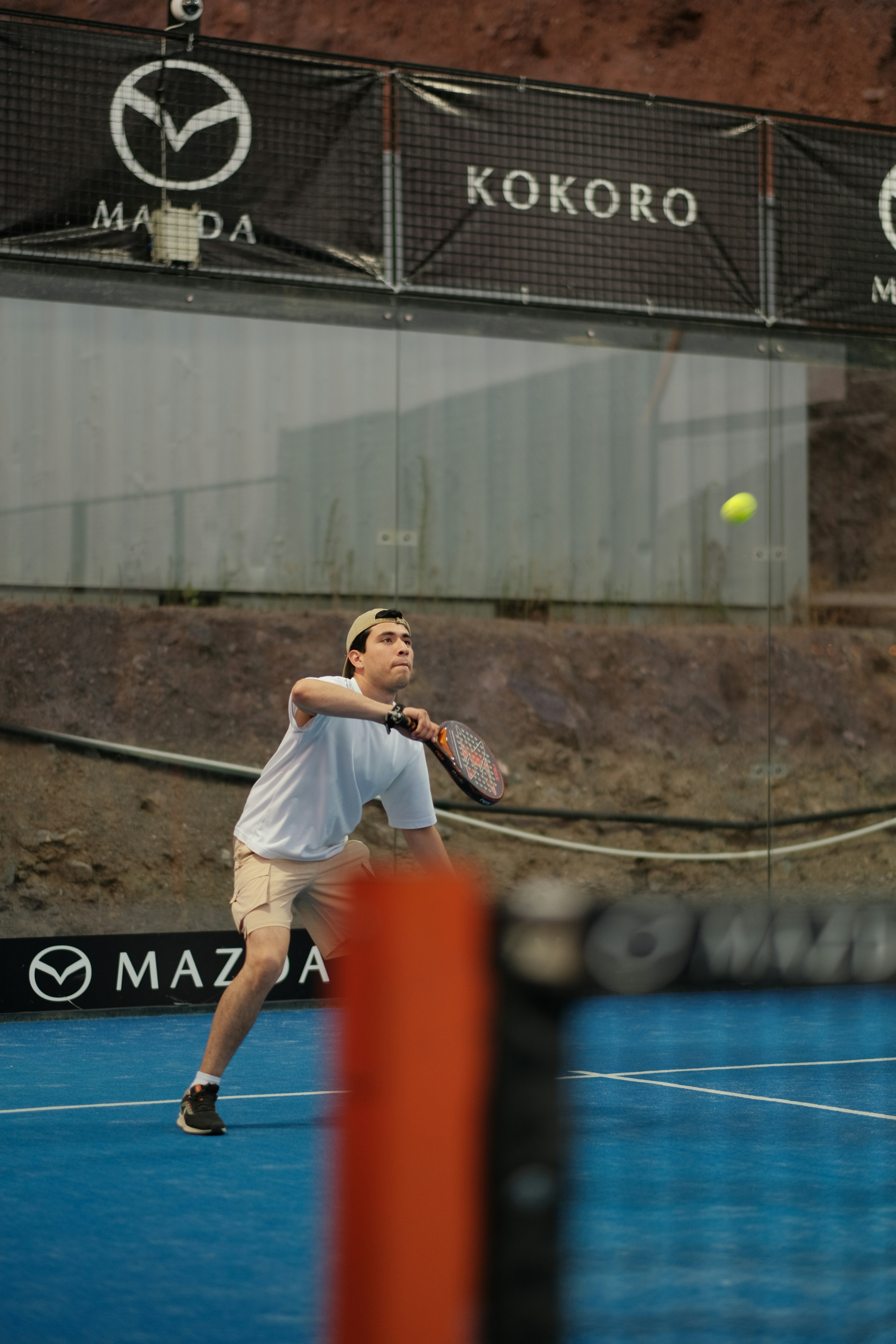 Mann spielt Padel, schlägt einen gelben Ball auf blauem Platz.