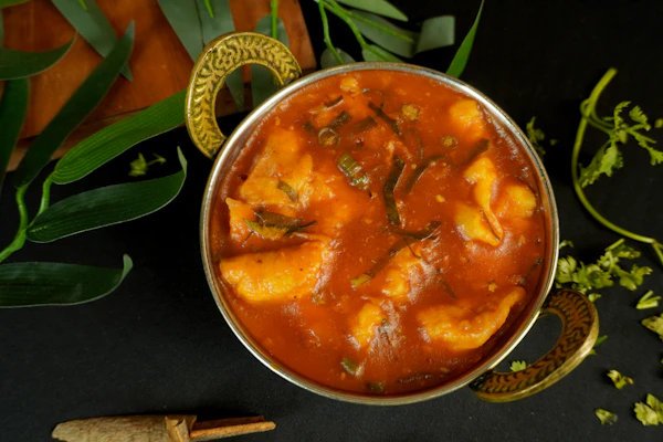 Prawn curry in a brass pot surrounded by leaves