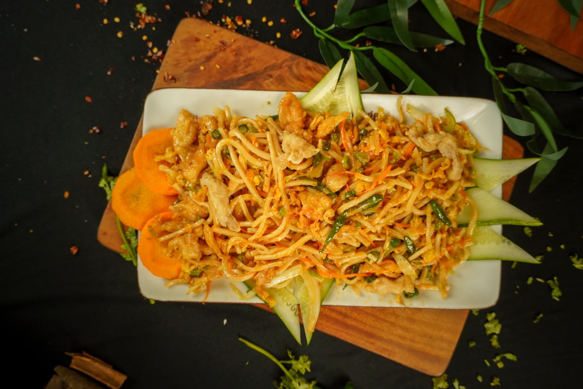 chinese chicken noodles with vegetables garnished with cucumber and carrots