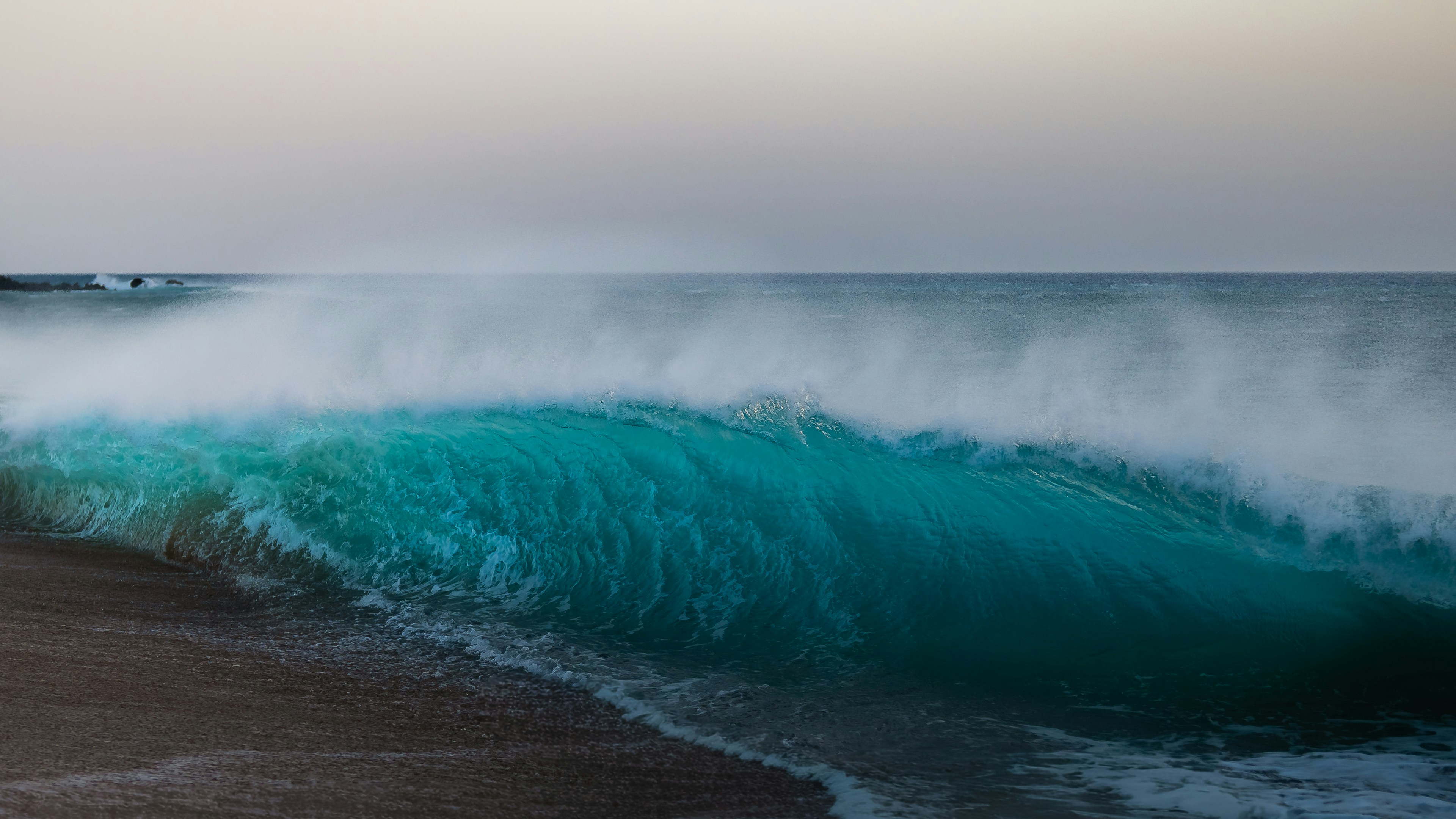 A large turquoise ocean wave breaking on a sandy beach