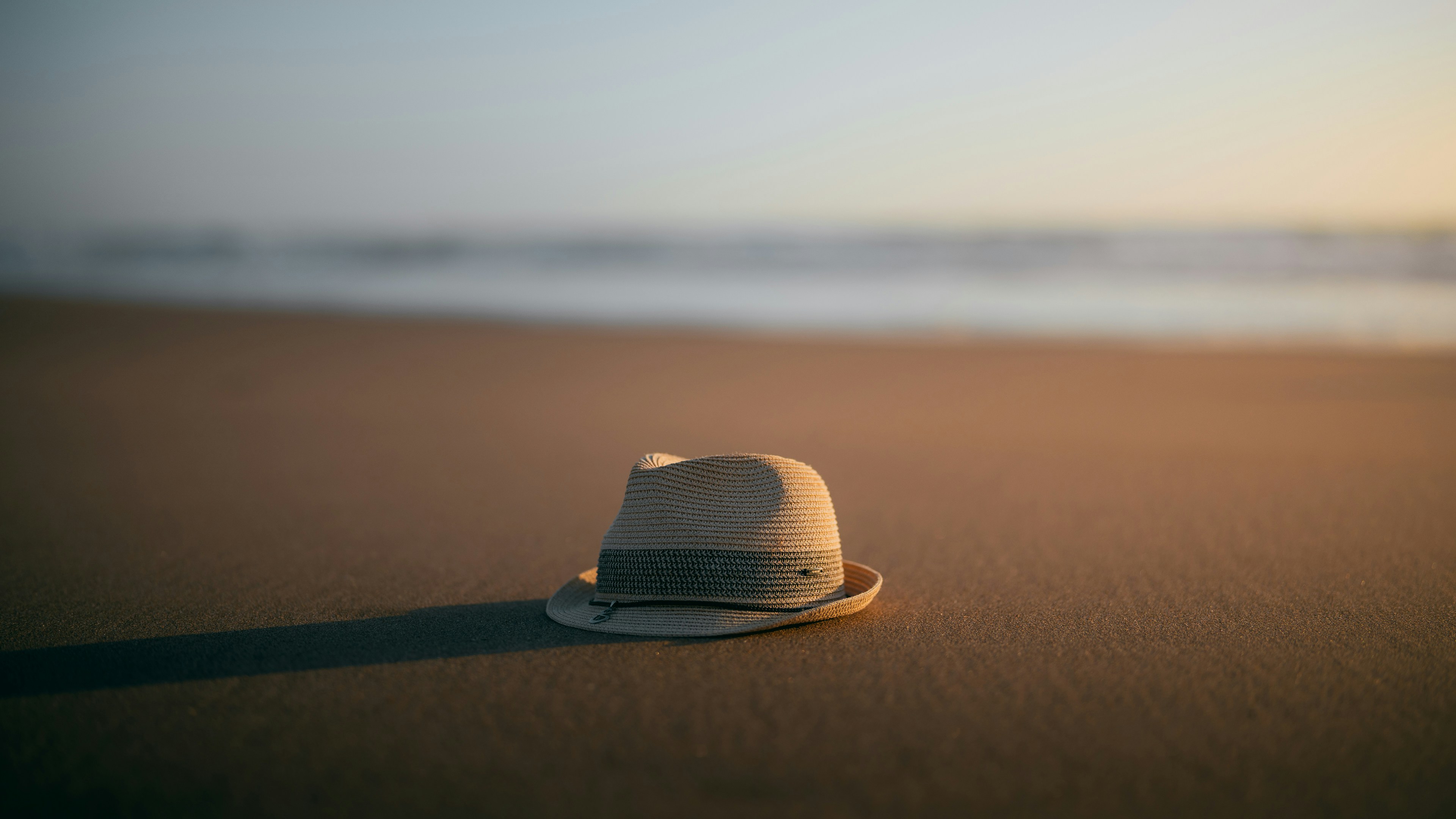A fedora hat lies on a sandy beach