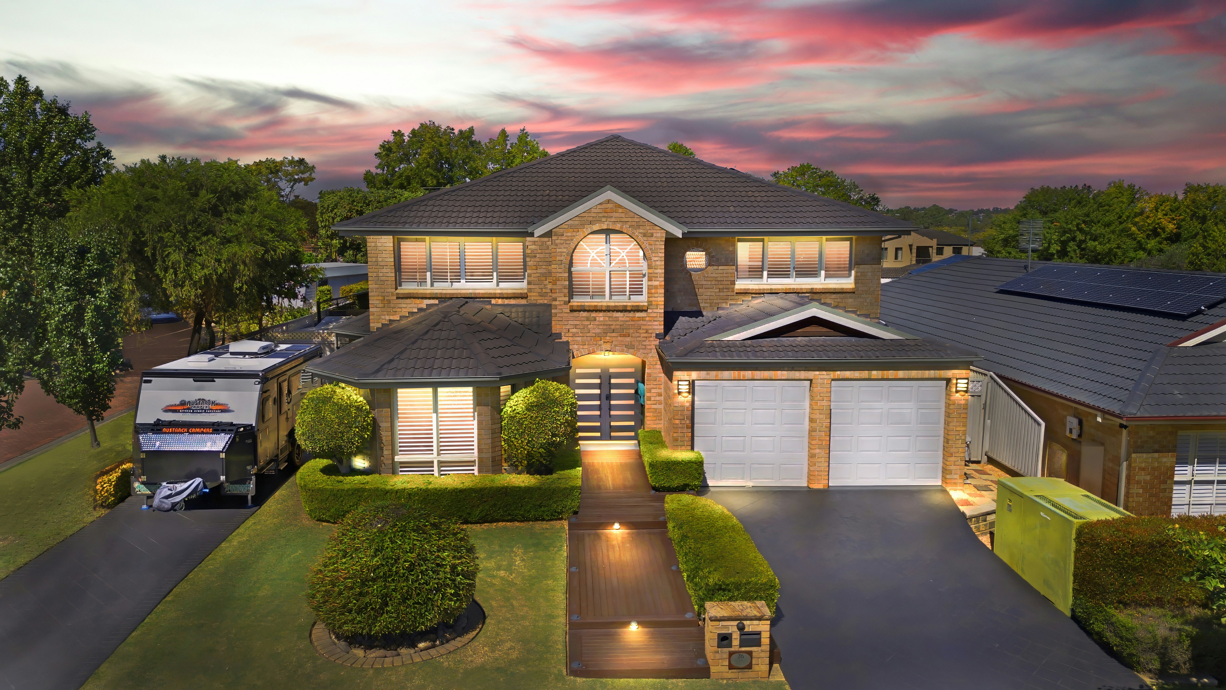 Large two-story house with illuminated pathway at dramatic sunset.