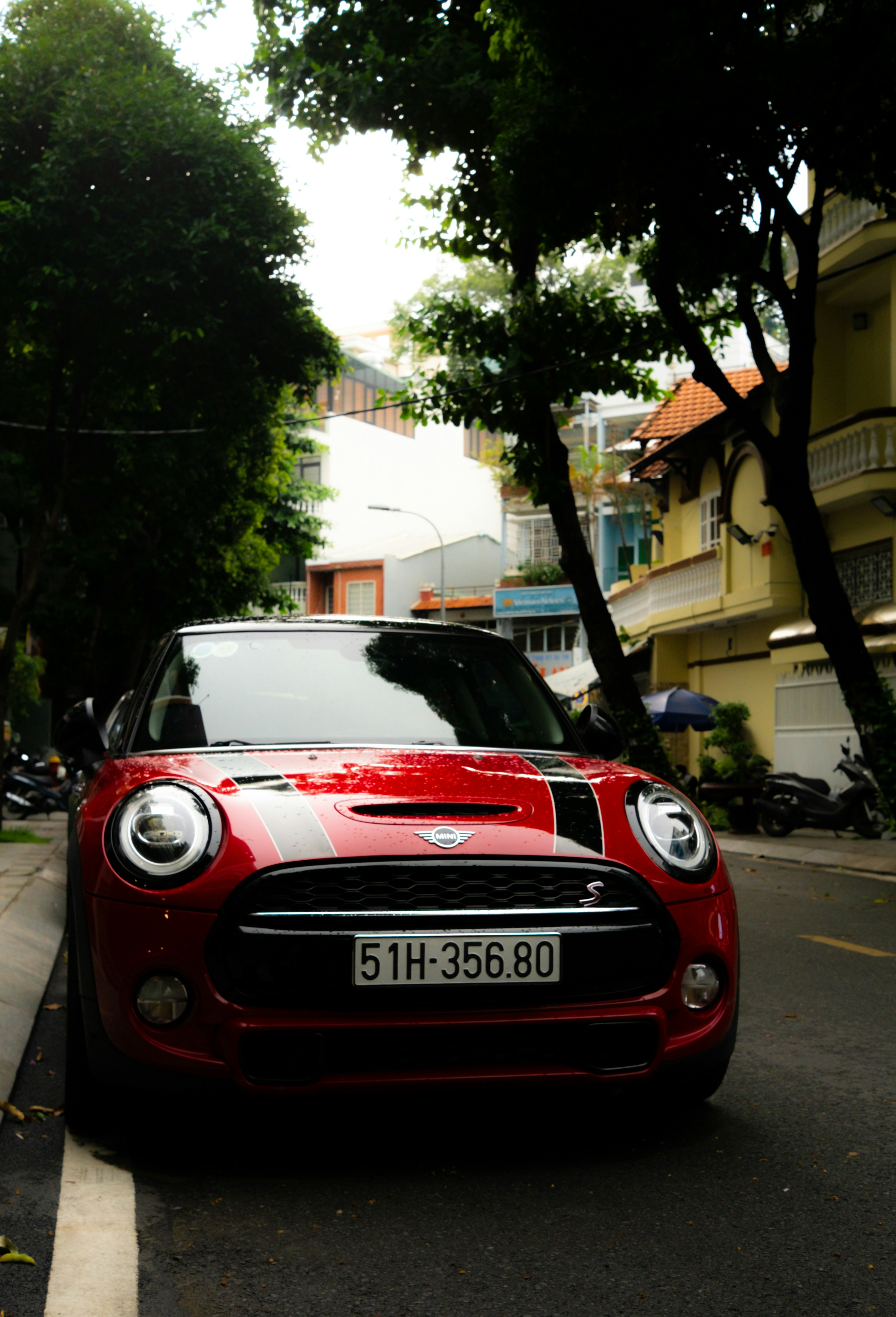 A red mini cooper car parked on a tree-lined street.
