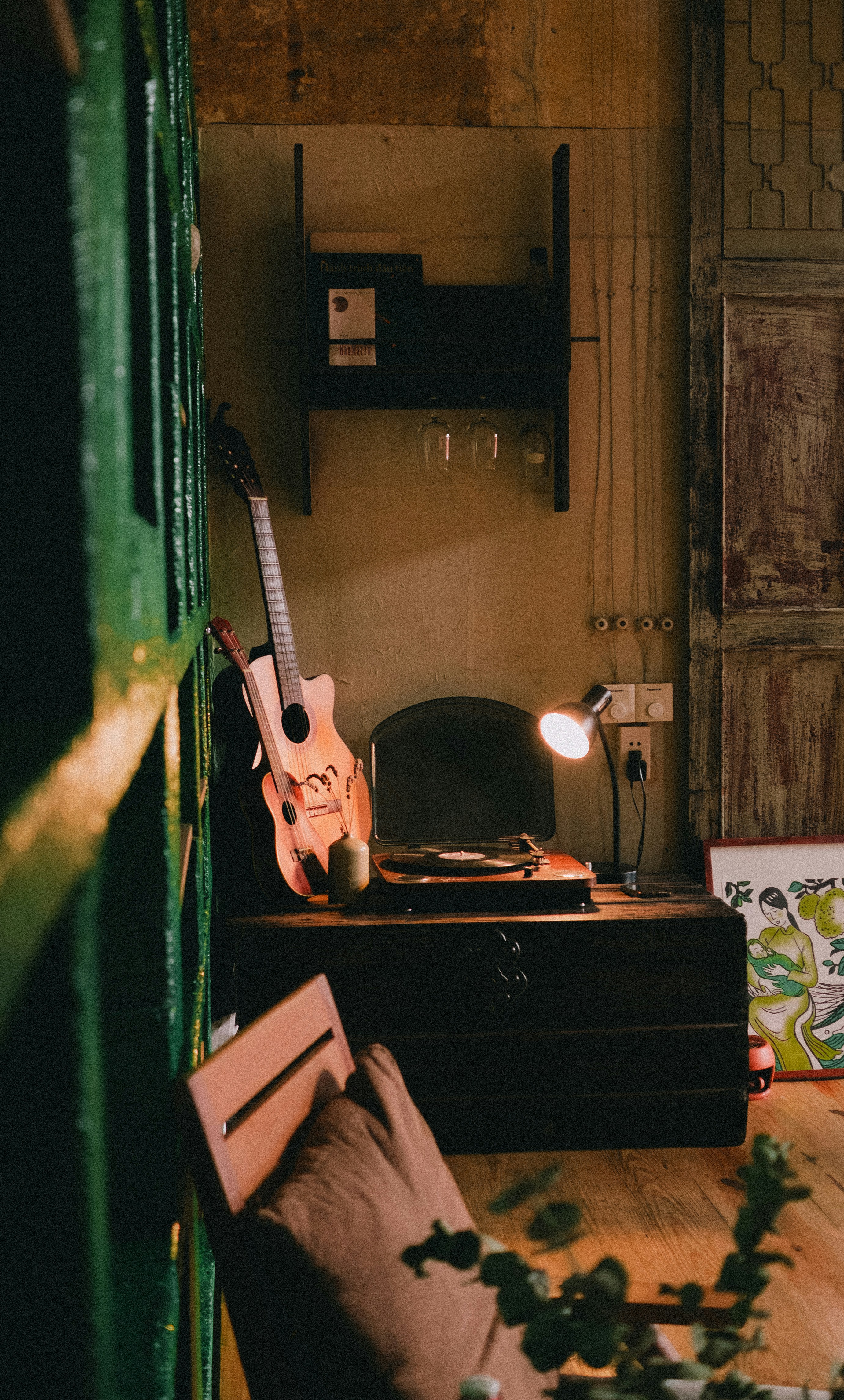 A guitar leans by a record player and glowing lamp.