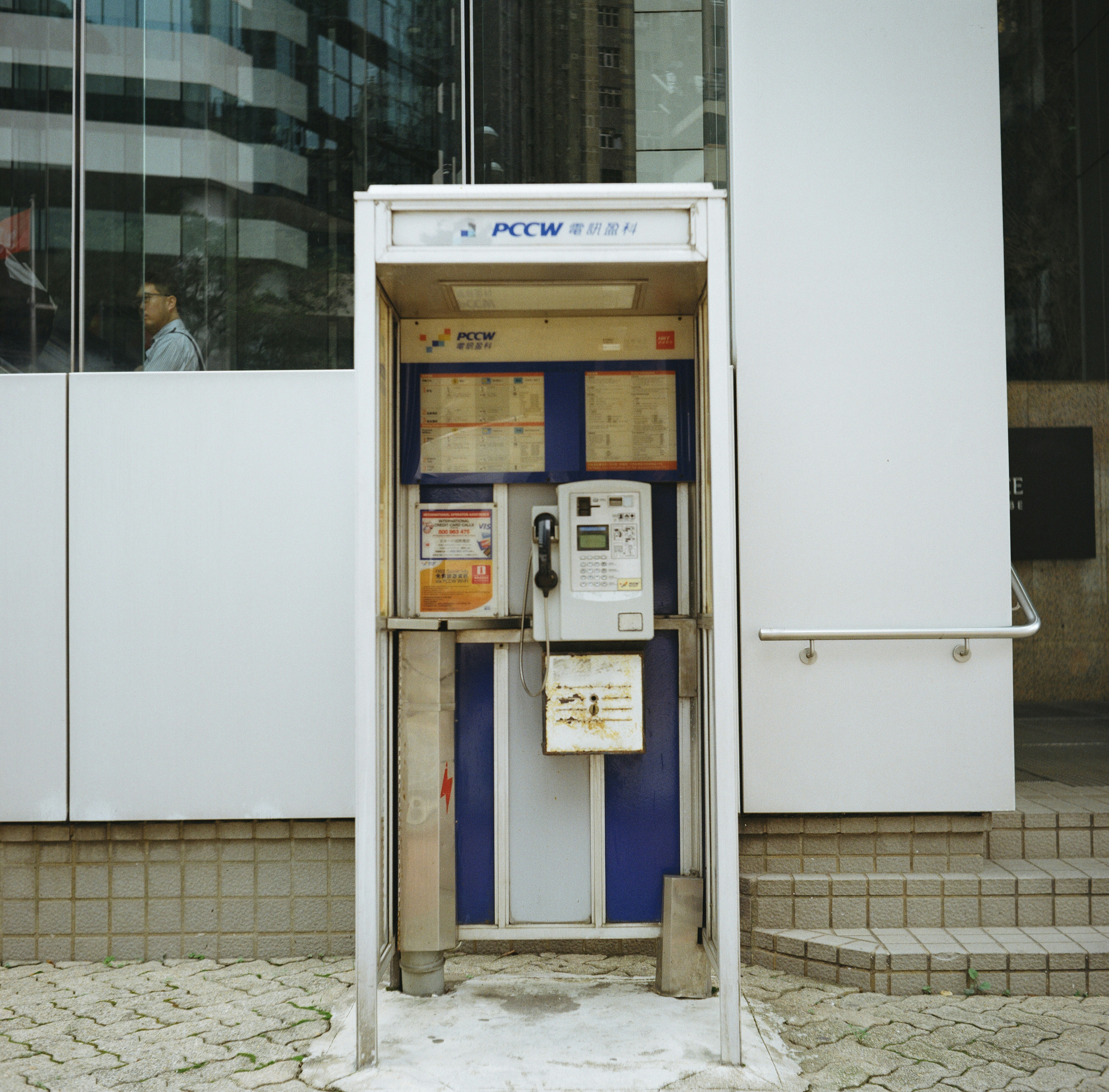 A public telephone booth stands on a city sidewalk.
